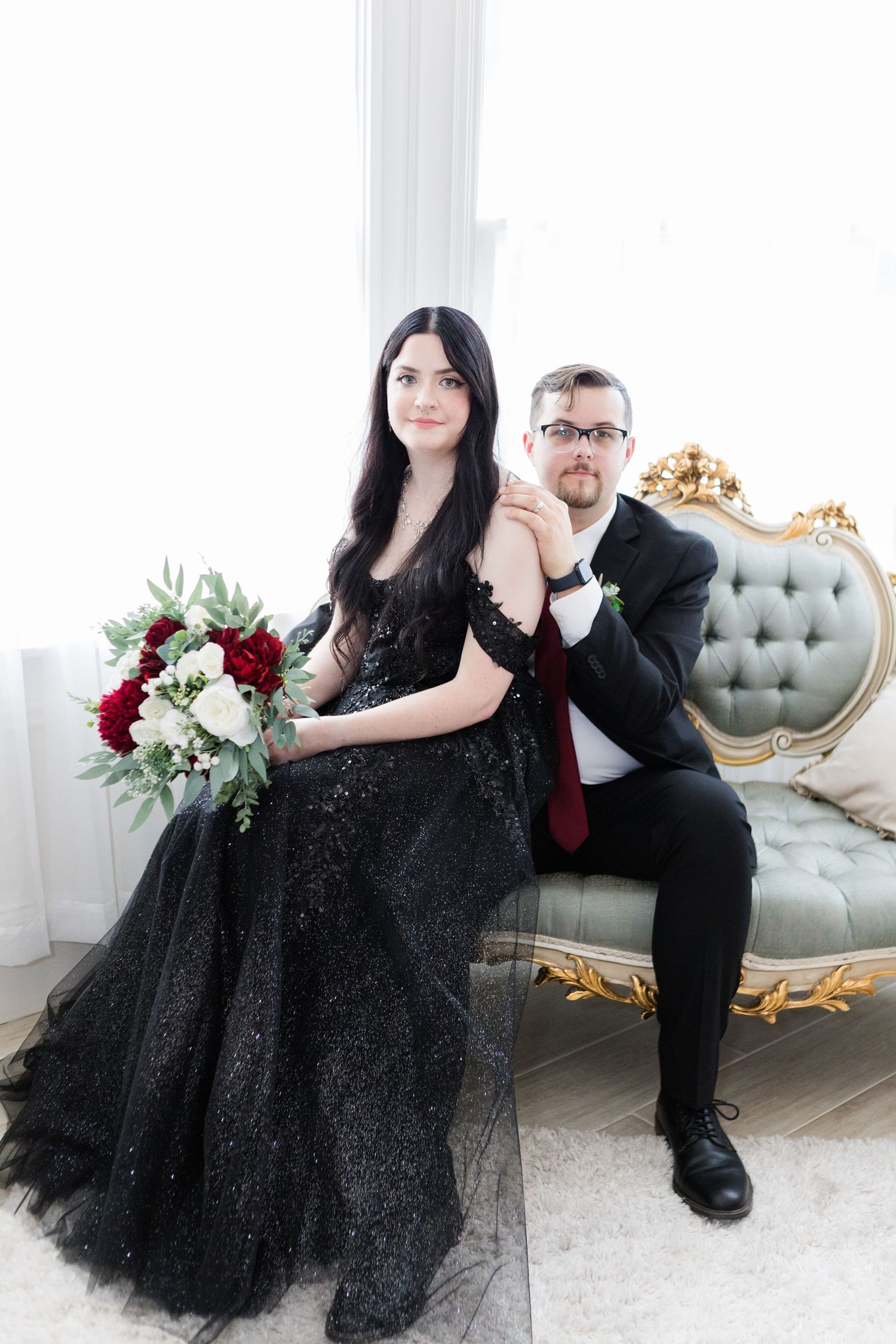 Wedding couple poses on ornate gray settee in elegant indoor setting.