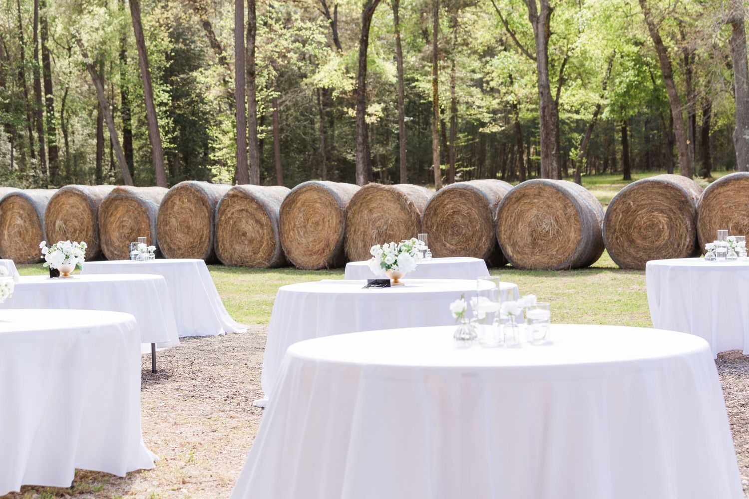 White-clothed reception tables arranged outdoors with rustic wooden barrels in the background.
