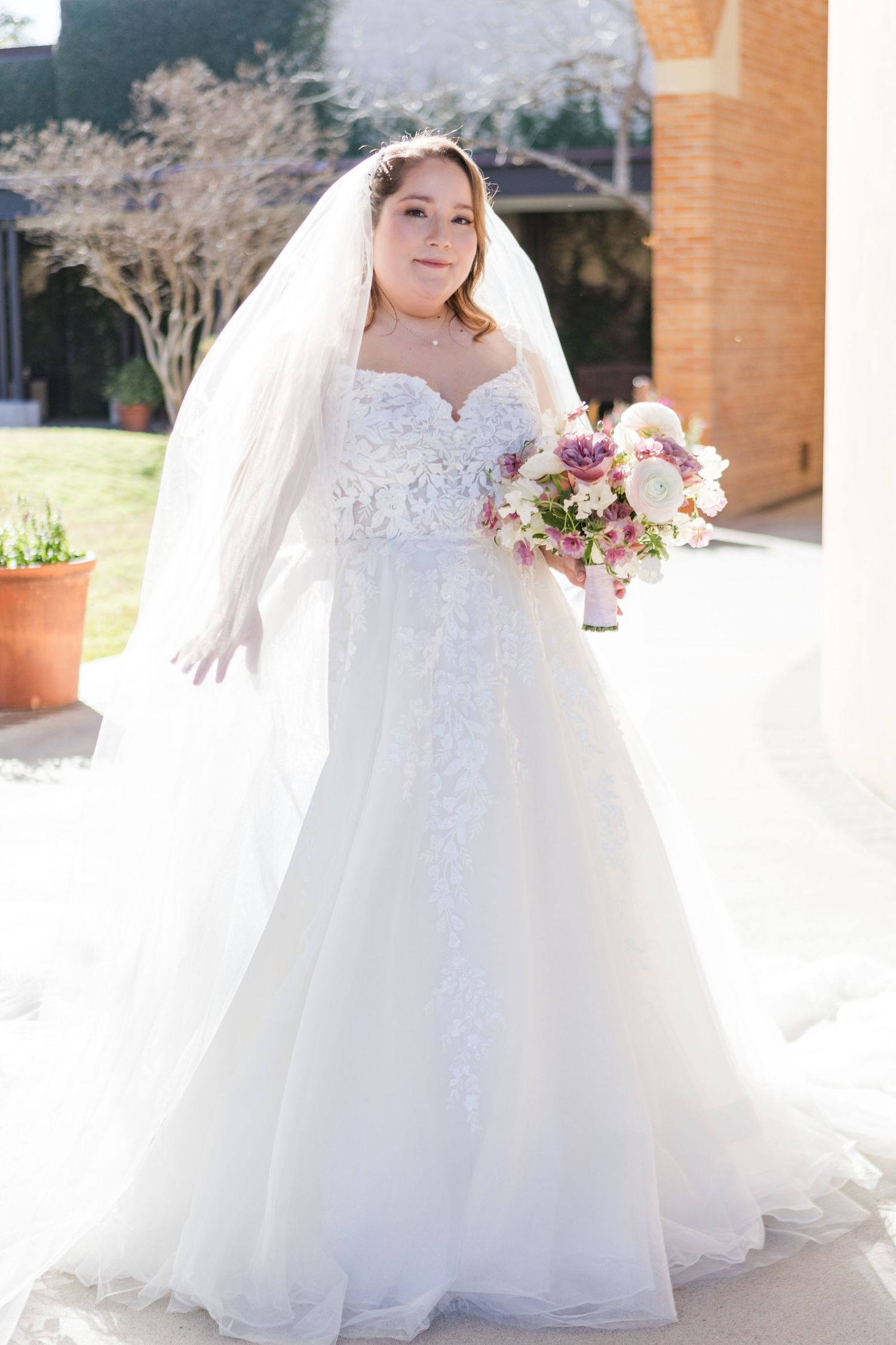 Beautiful bridal portrait showcasing a flowing white wedding gown and delicate floral bouquet in outdoor setting.