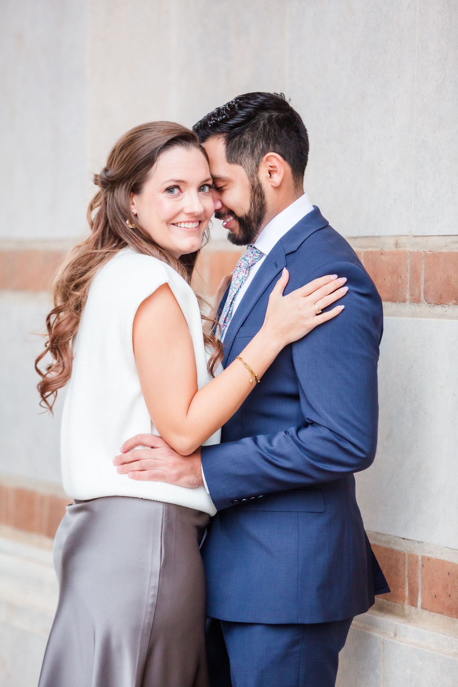 Candid romantic moment captured against white wall with terra cotta architectural details.