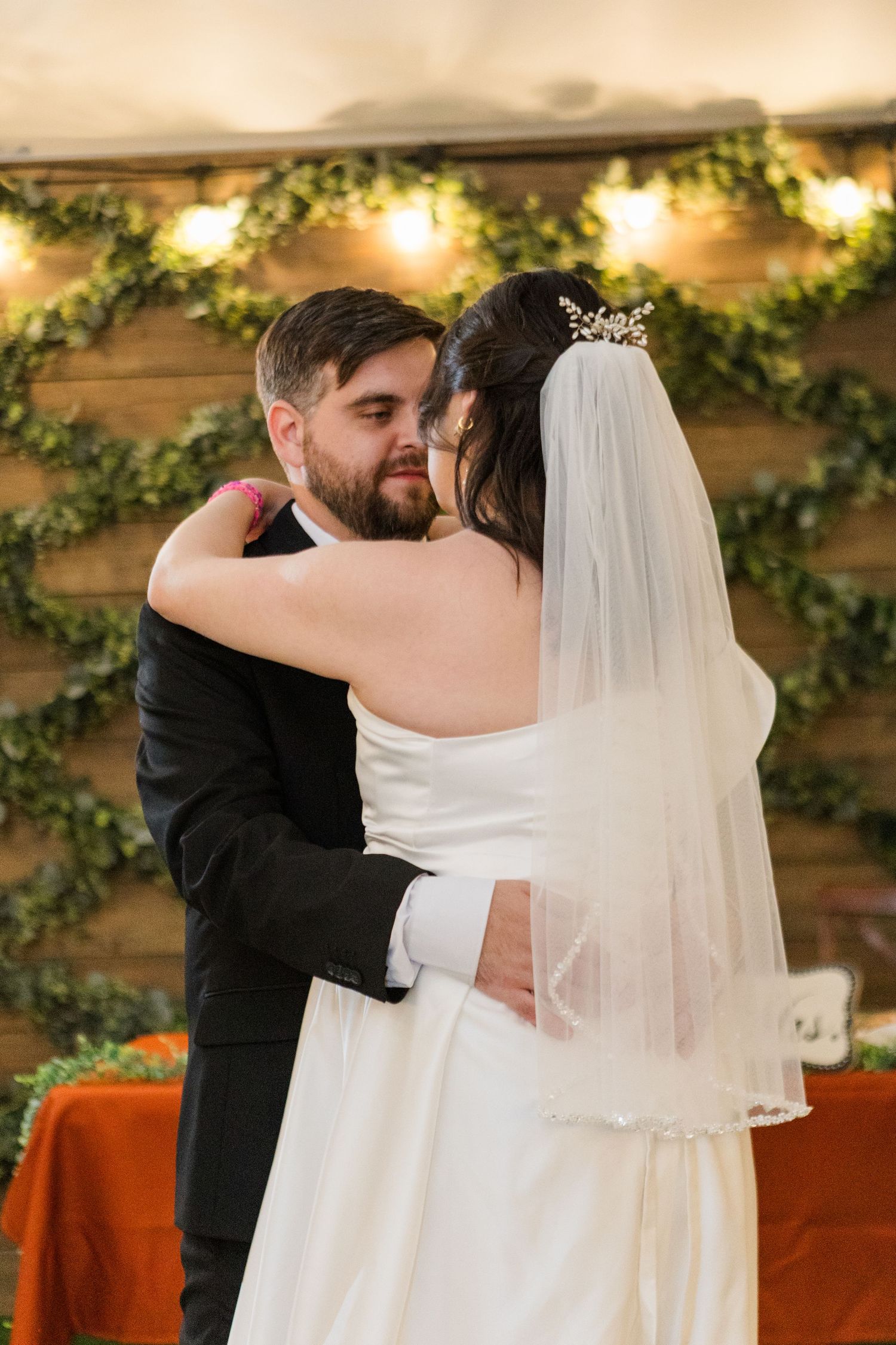 A tender first dance moment between newlyweds at a rustic wedding venue decorated with greenery and warm lighting.