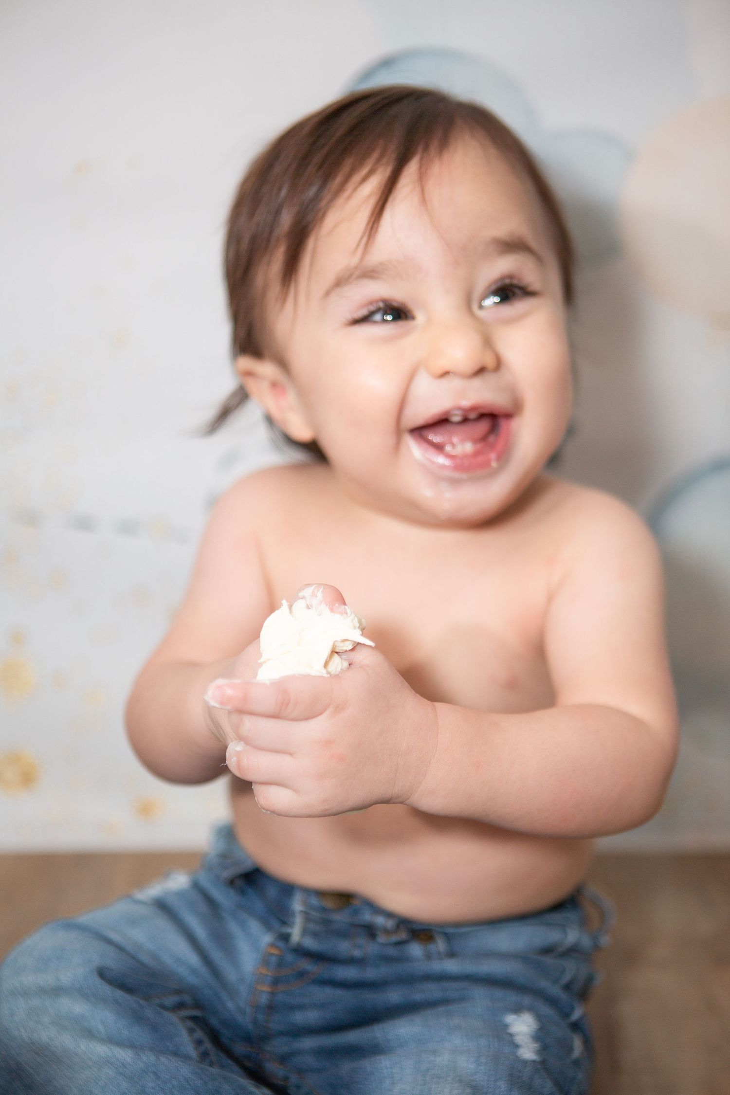 Happy baby wearing denim enjoying messy cake smash with white frosting.