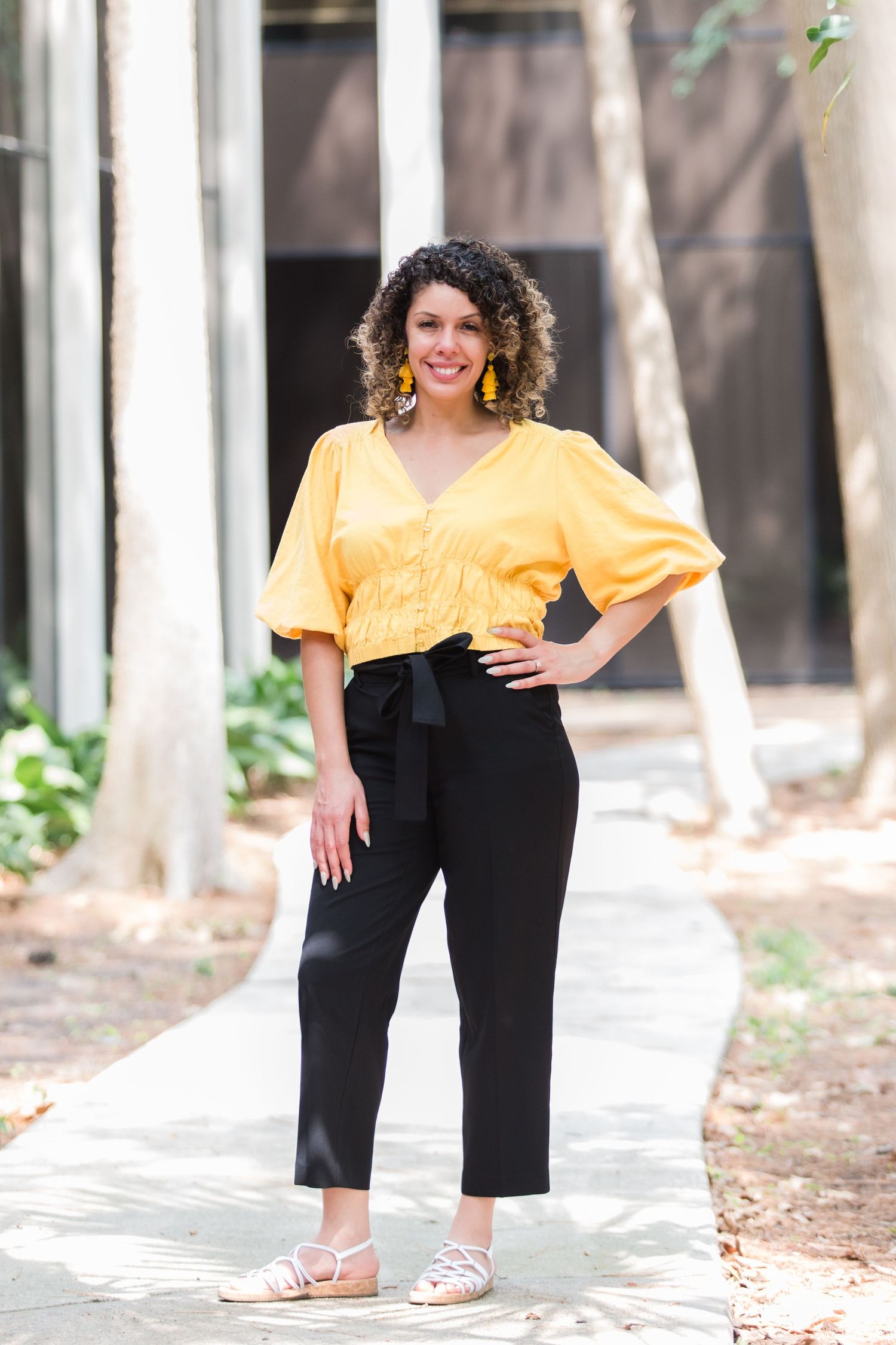 Woman in yellow top and black pants poses outdoors for casual portrait series.