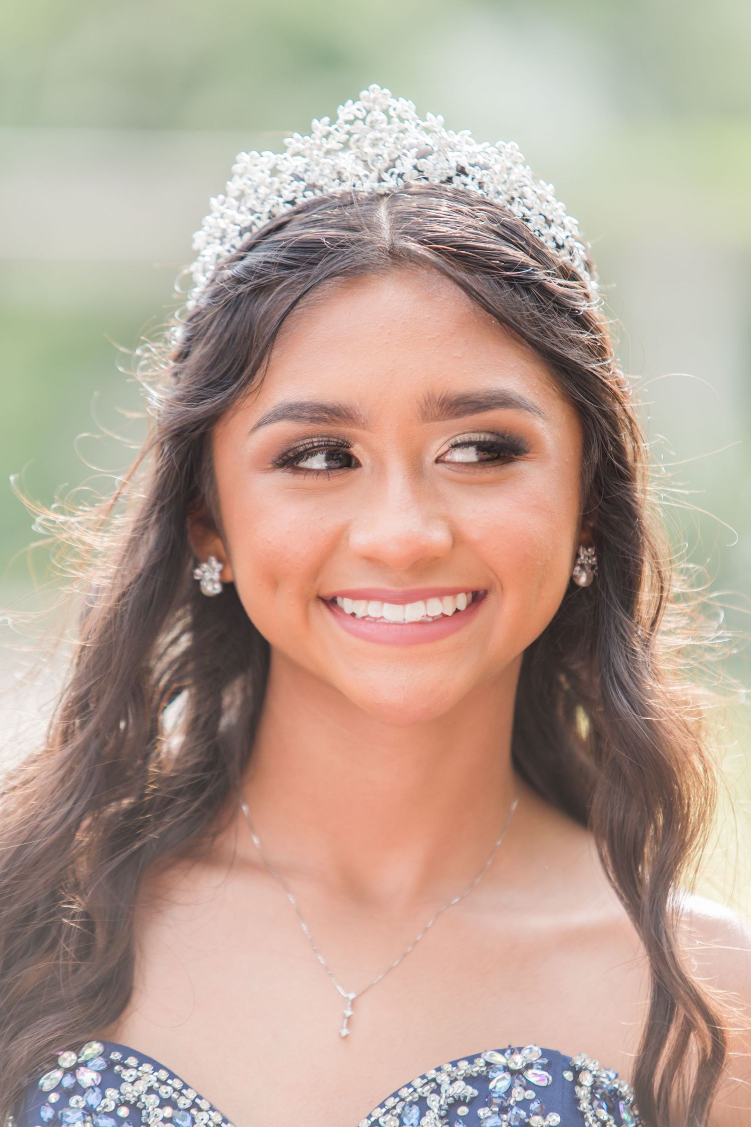 Close-up portrait showing a delicate crystal tiara and sparkling jewelry against a soft natural background.