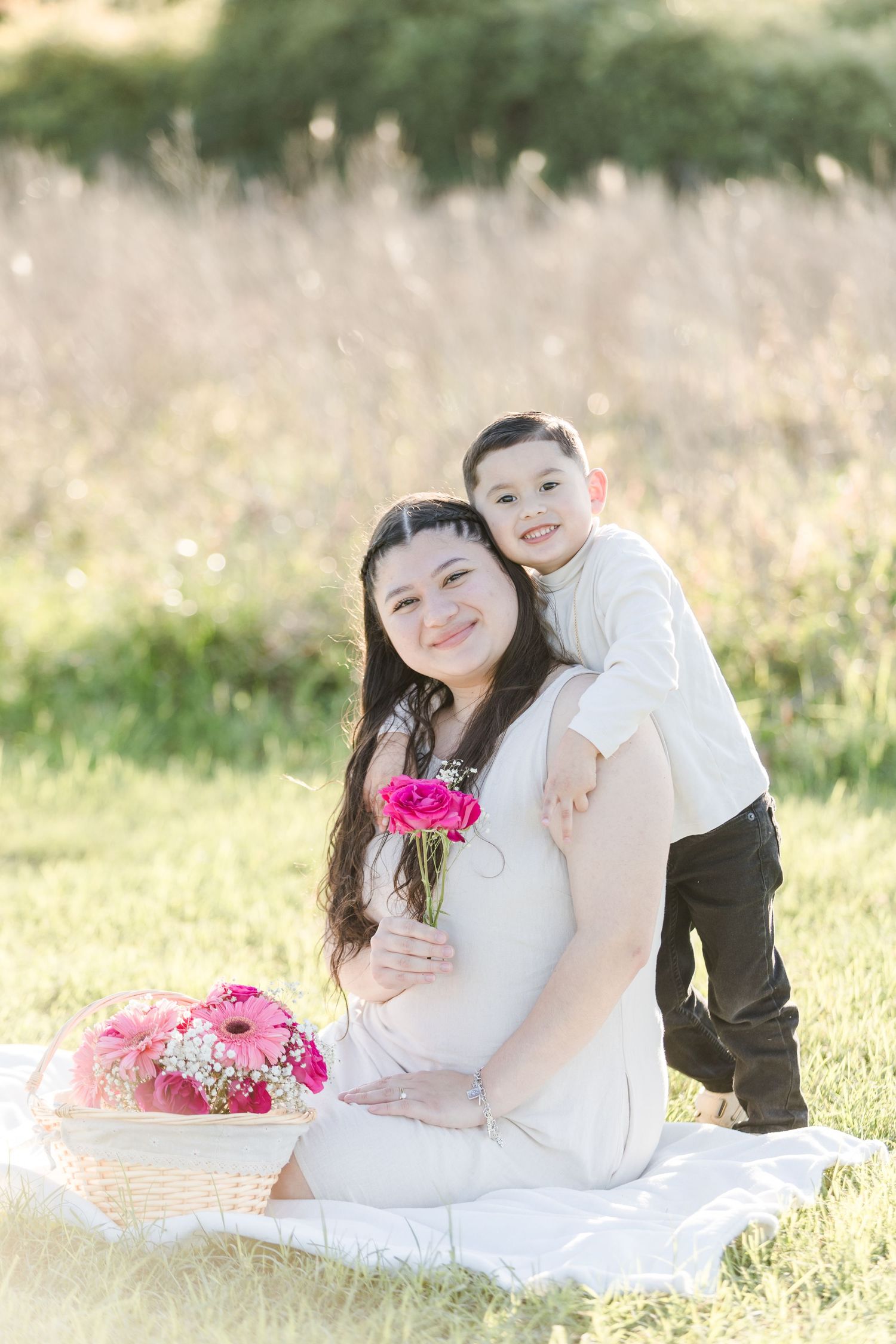 Couple in white outfits sharing tender moments with pink flowers in a sunlit meadow setting.