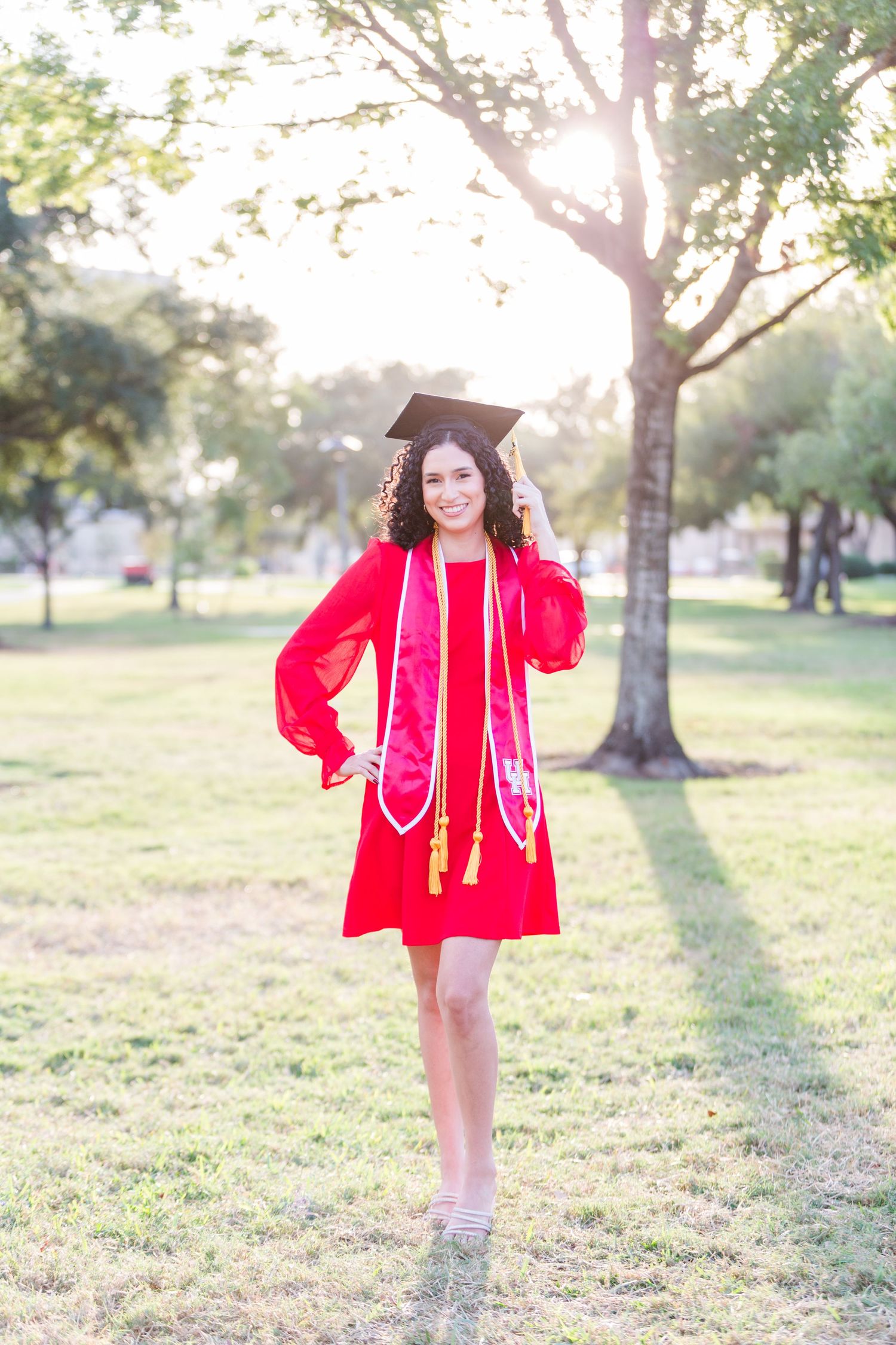 Person in bright red dress twirling outdoors in sunlit park setting.