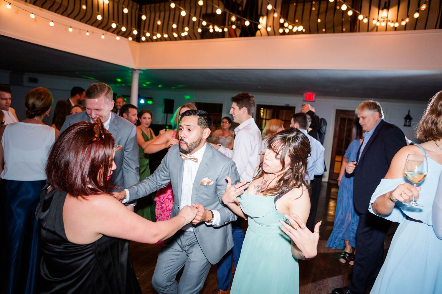 Wedding guests dance joyfully on a crowded reception dance floor under ambient lighting.