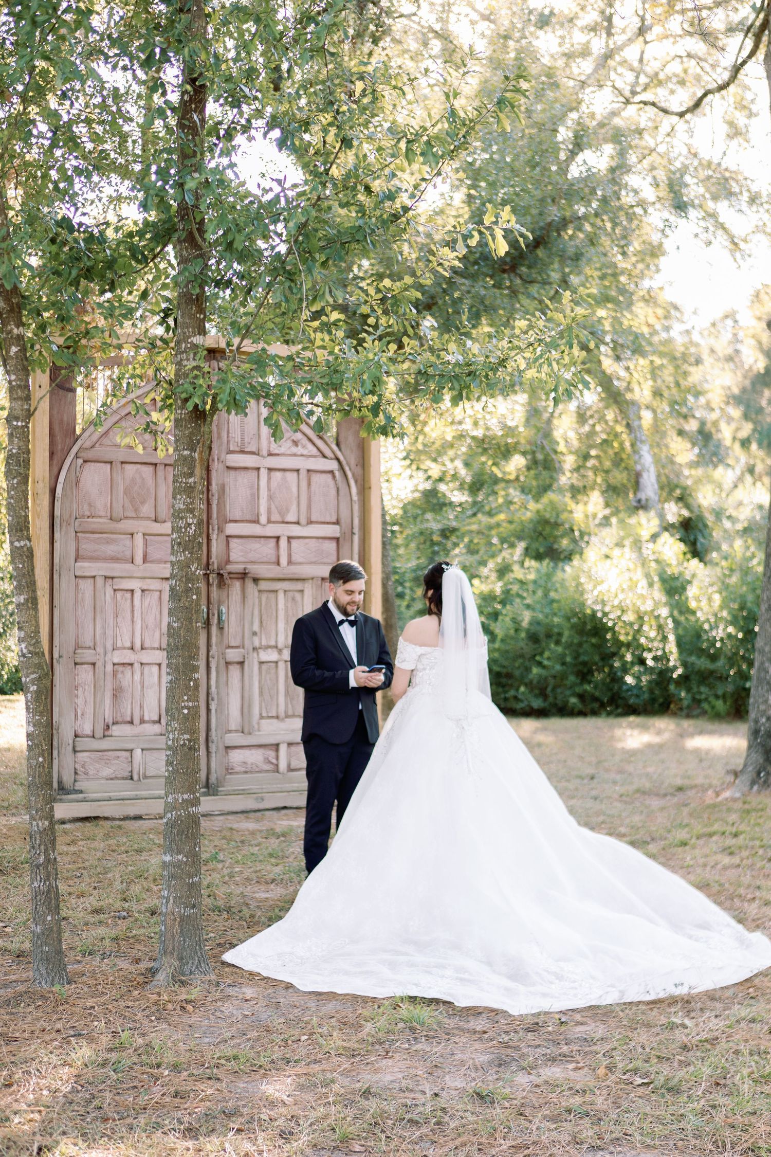 Elegant outdoor wedding scene with vintage wooden doors and natural greenery backdrop.