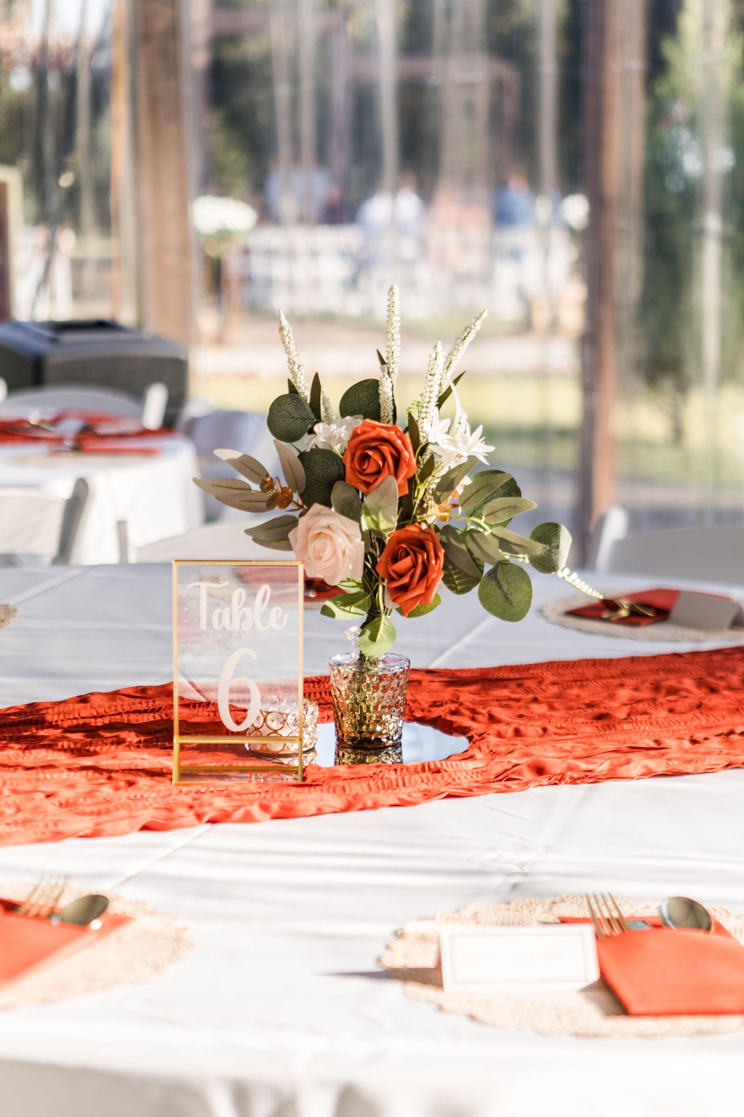 Wedding reception table settings with orange accents, white linens, and floral centerpieces.