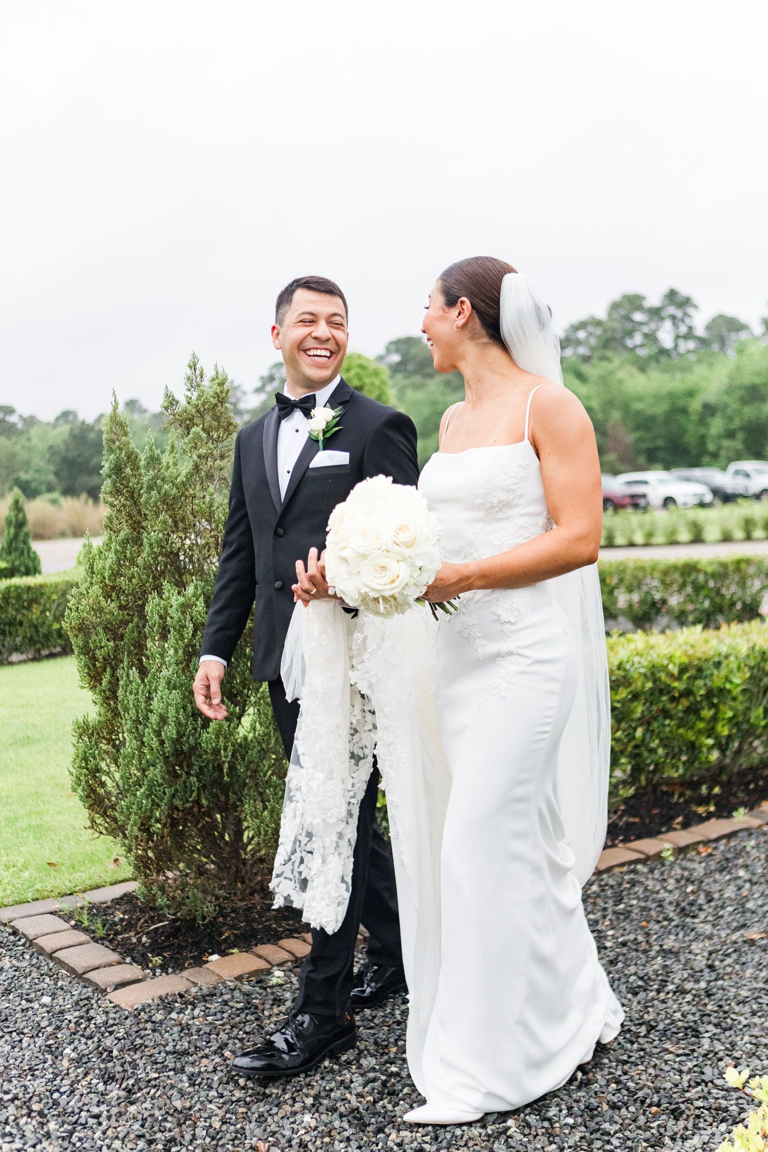A couple shares a joyful moment in formal attire in a garden setting.
