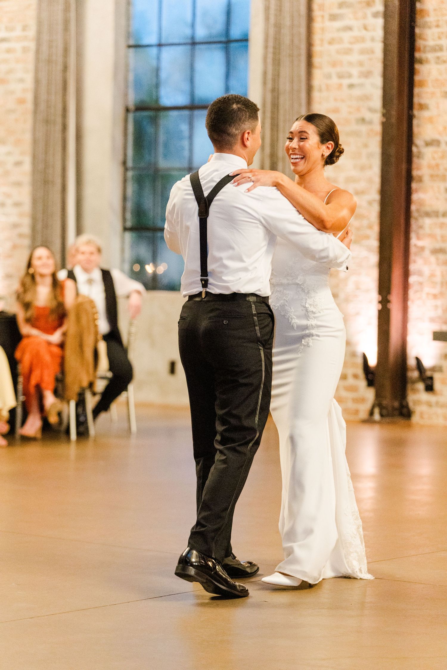 Wedding couples share intimate dance moves in a rustic reception venue with brick walls.