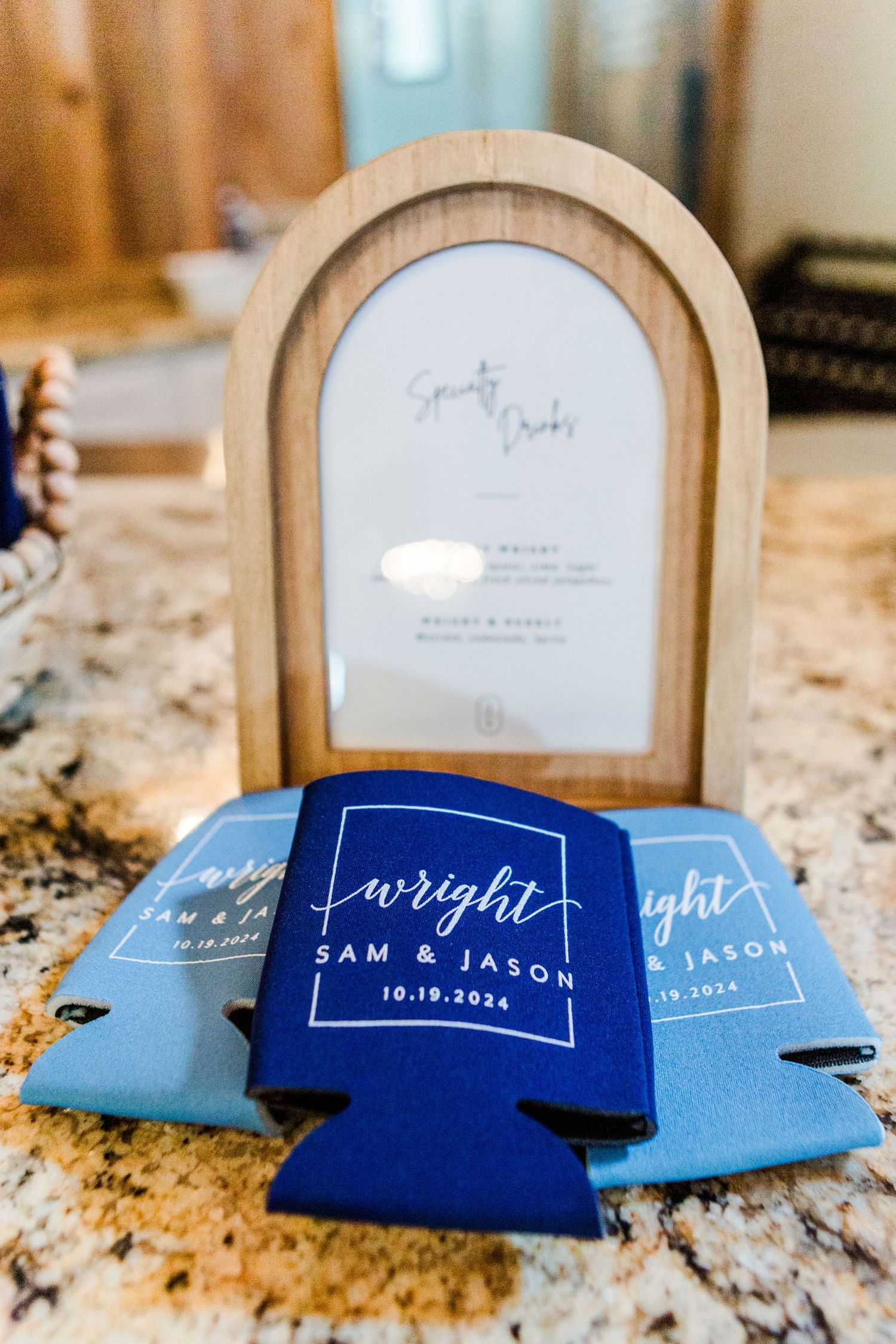 Blue wedding koozies with names and date displayed on wooden frames.