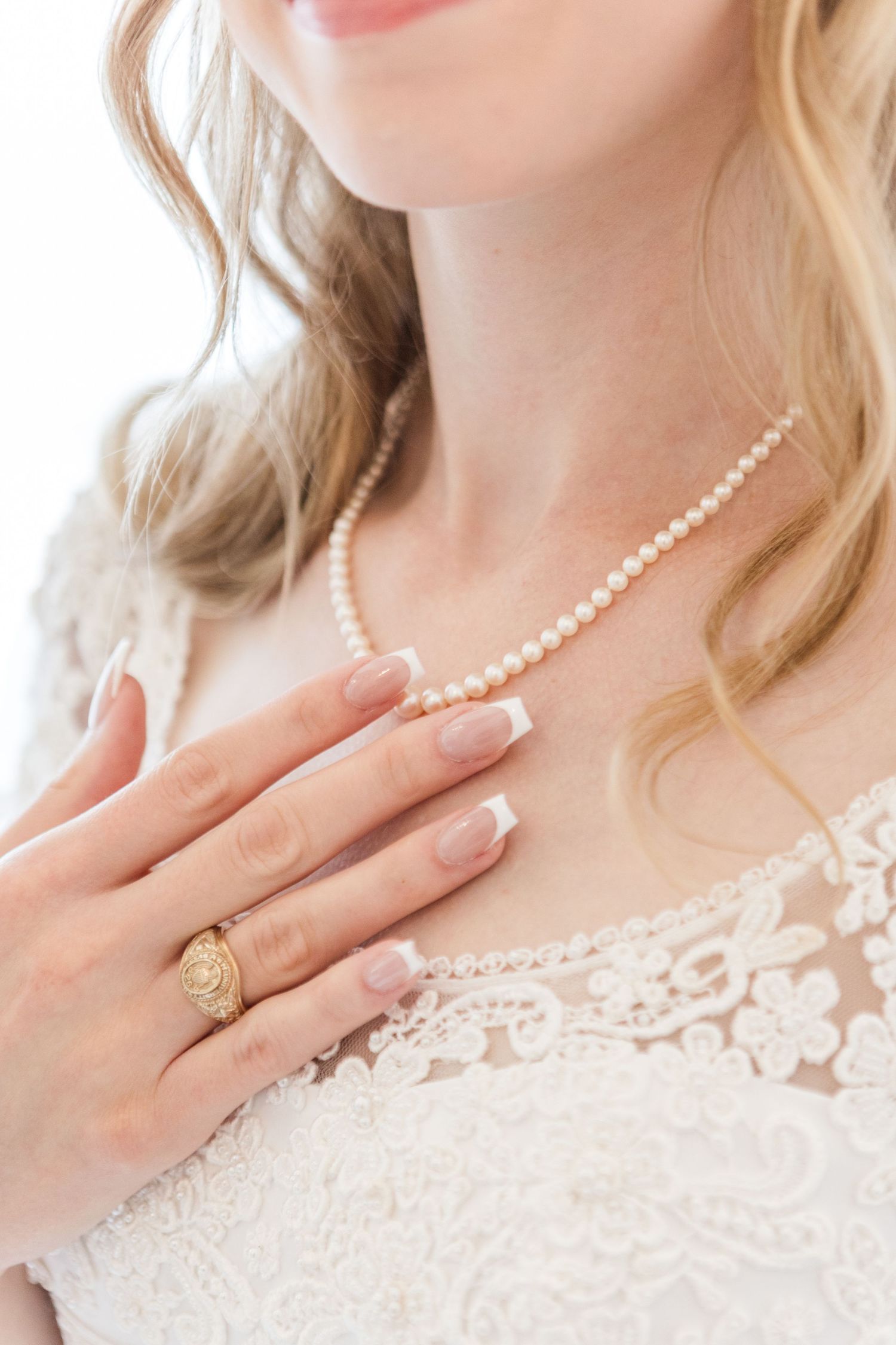 Elegant pearl necklace and ring details against white lace bridal attire.