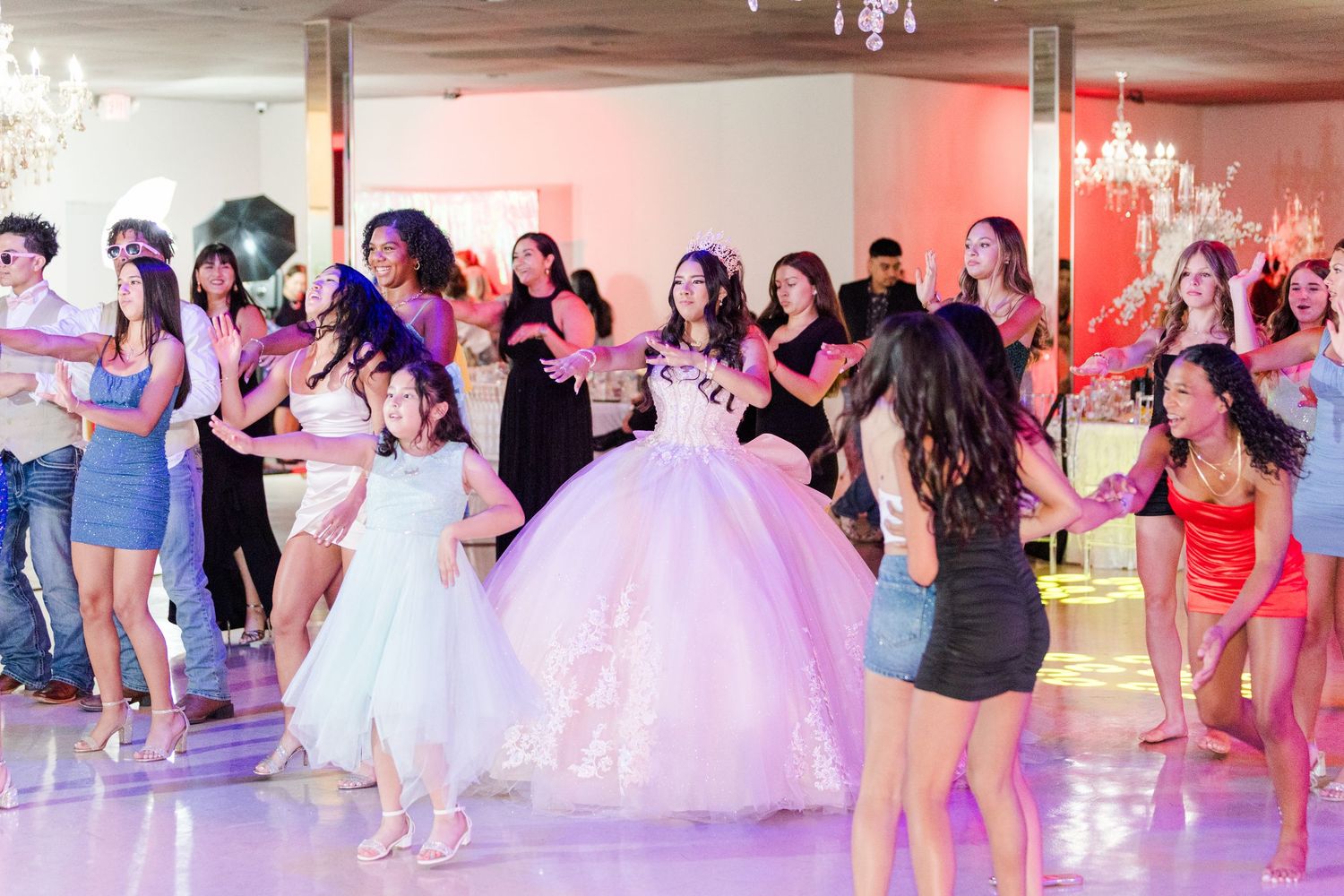 Celebration dance floor filled with party guests under crystal chandeliers with pink and purple lighting.
