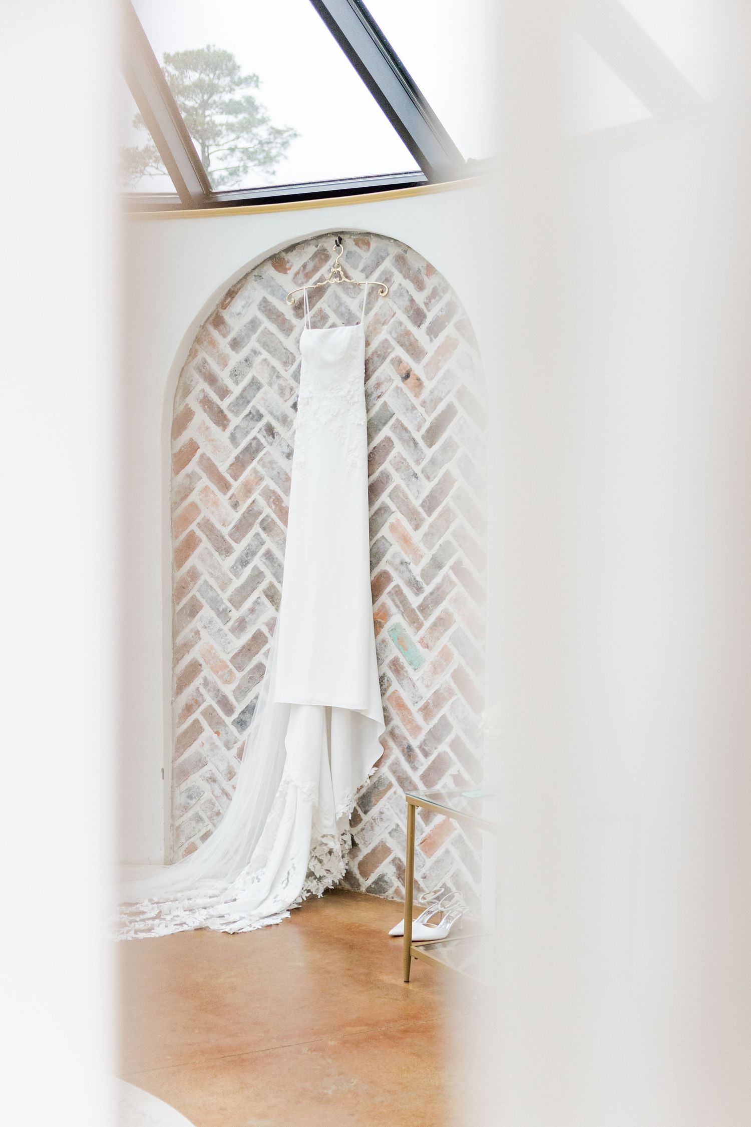White wedding gown hangs elegantly against herringbone brick archways in bright natural light.