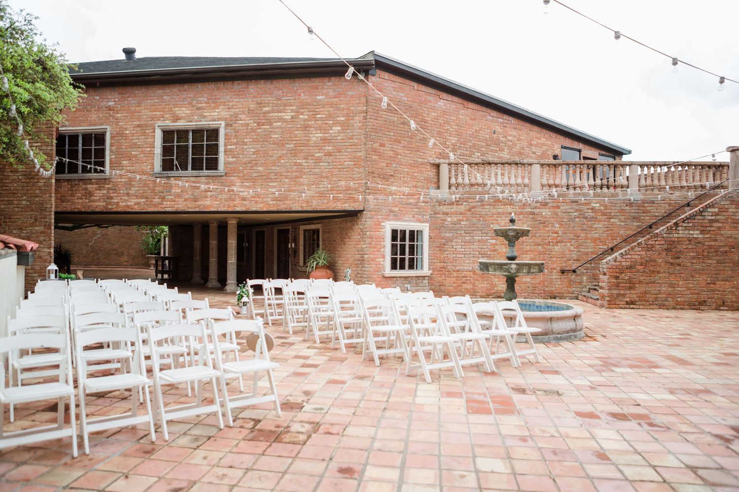 Rows of white chairs set up for an outdoor event against a brick building backdrop.