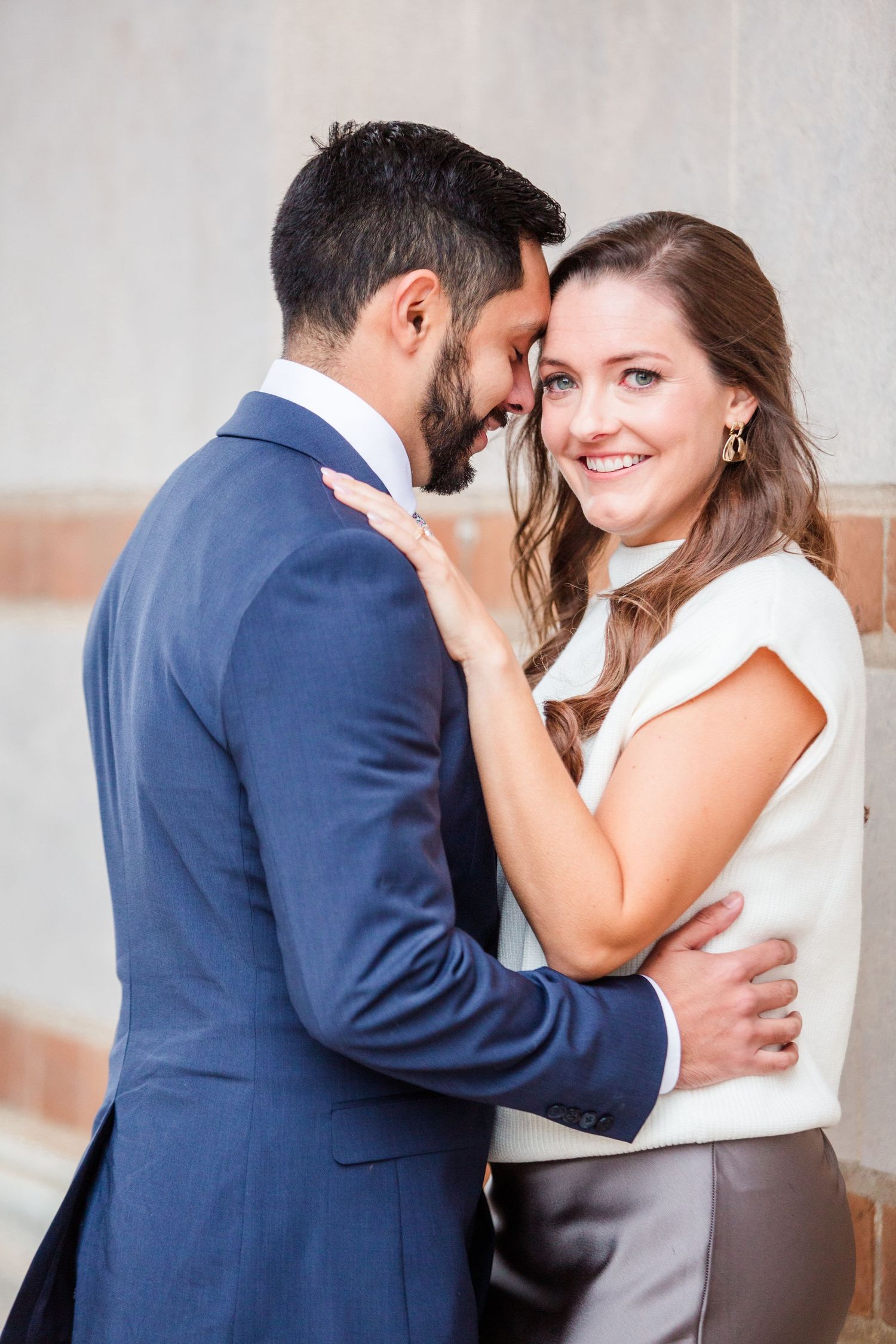 Intimate couple's portrait session showing genuine emotion against light stone wall backdrop.