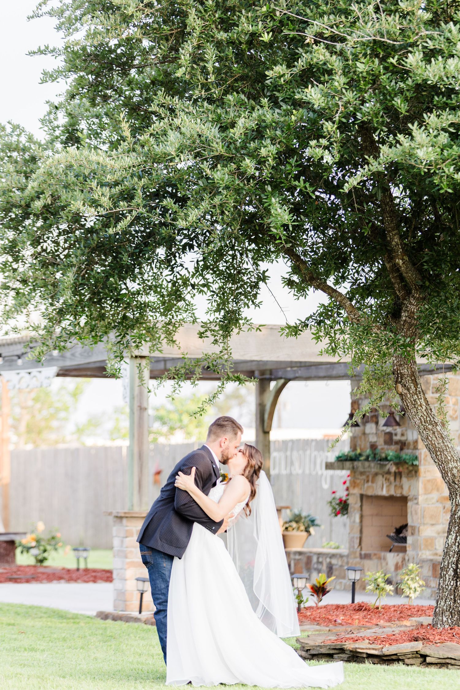 A sweet dance unfolds beneath leafy trees in a manicured backyard setting.
