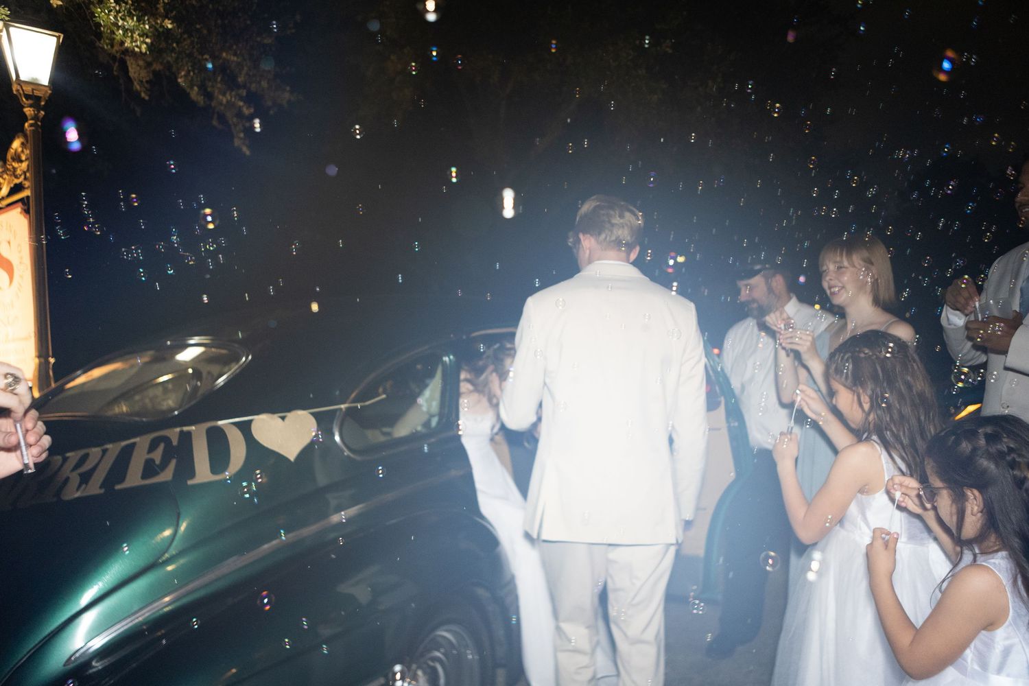 Wedding guests celebrating and dancing outdoors at night under twinkling lights.