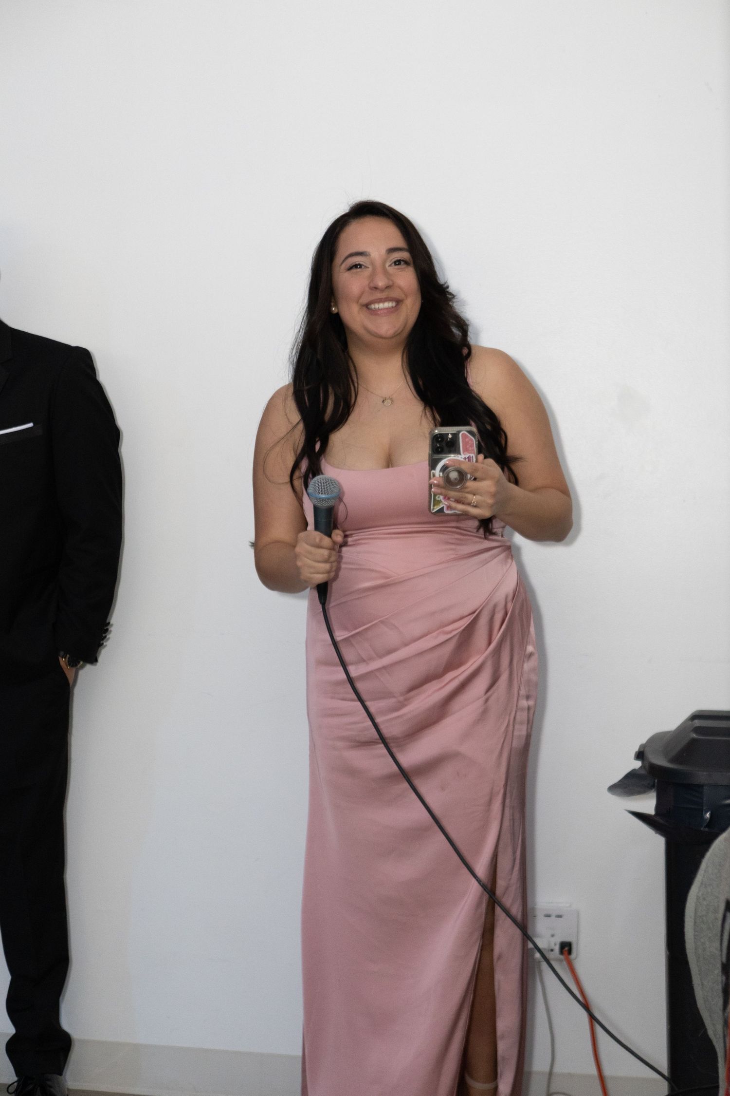 Person in pink formal dress holding microphones against white backdrop.
