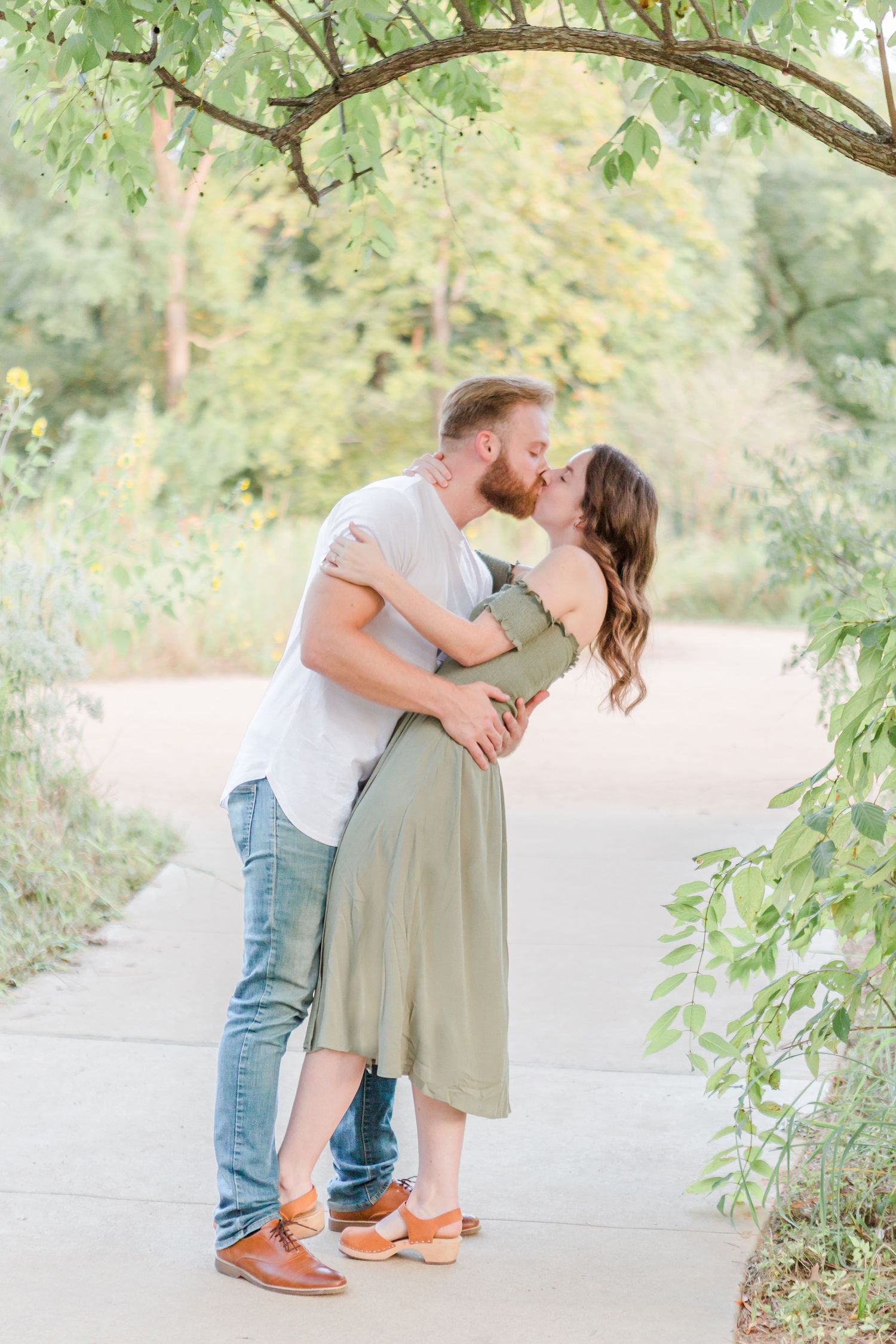 Romantic outdoor engagement photoshoot in a natural setting with soft lighting and green foliage.