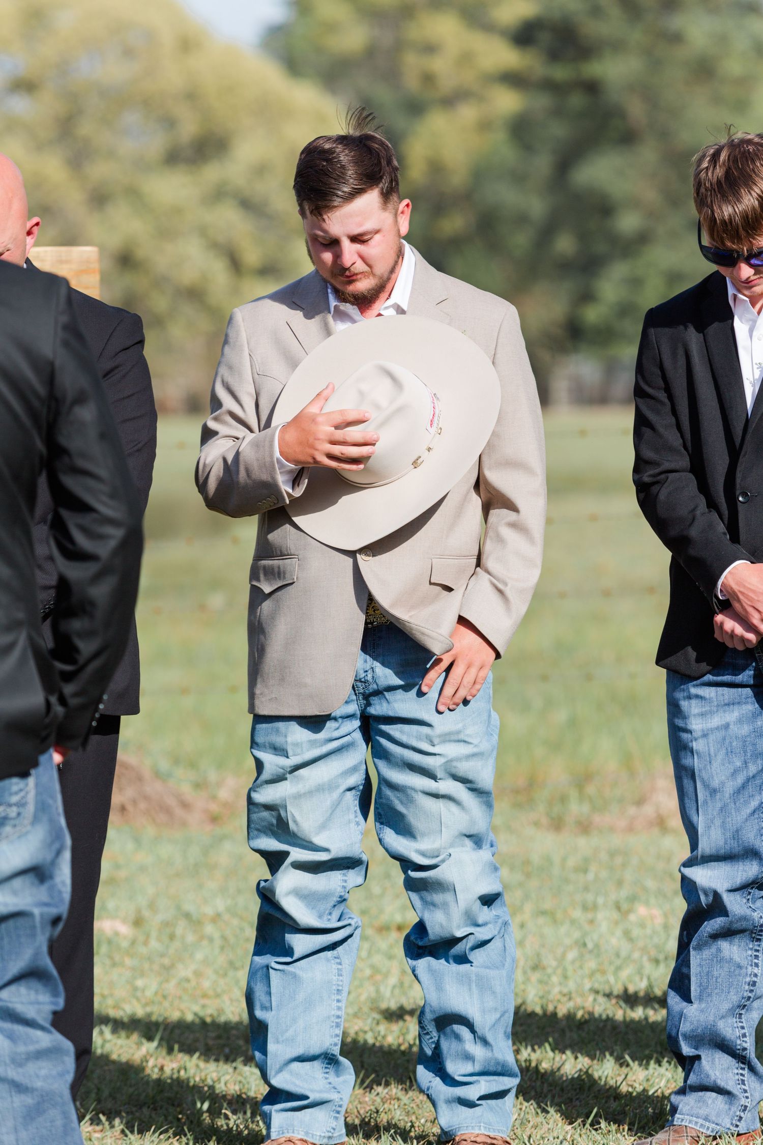 Wedding party members in casual country attire stand in a grassy field.