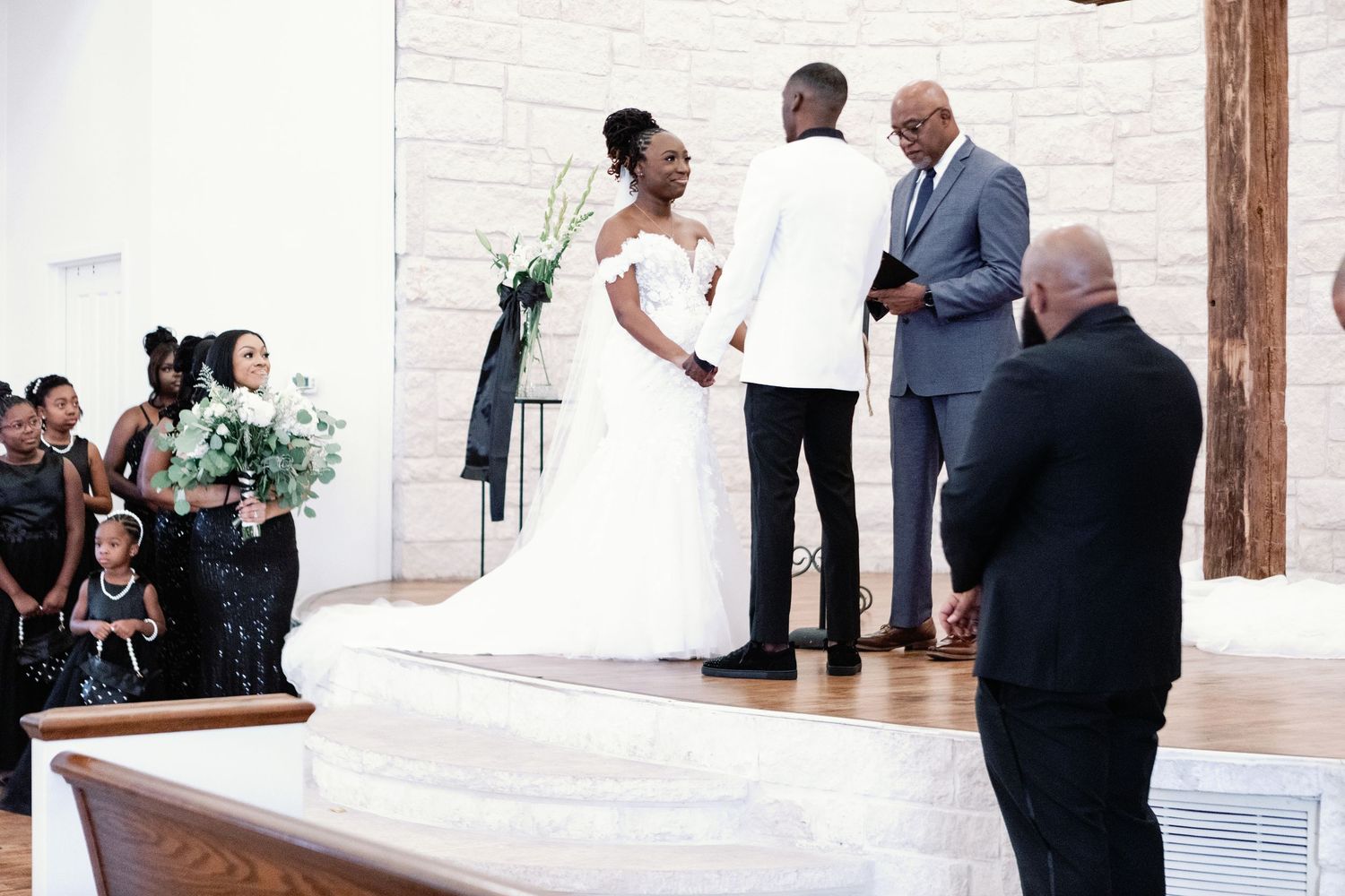 A romantic wedding couple shares their first dance in an elegant white ballroom venue during their reception.