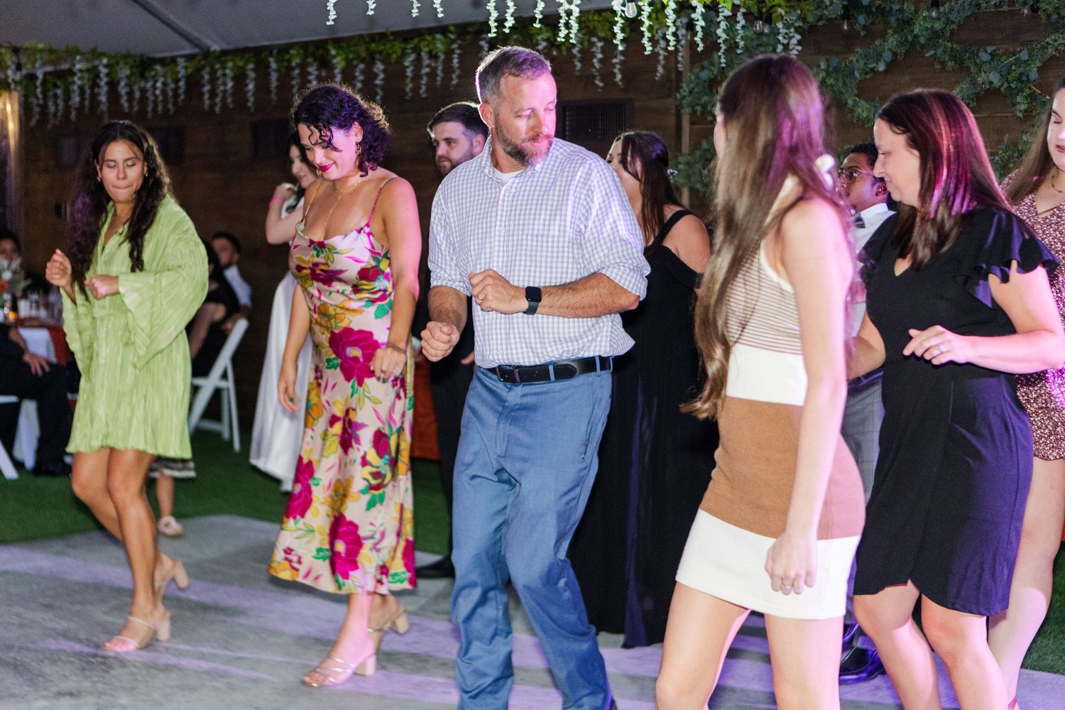 Wedding guests dancing and celebrating on outdoor reception dance floor with festive lighting.