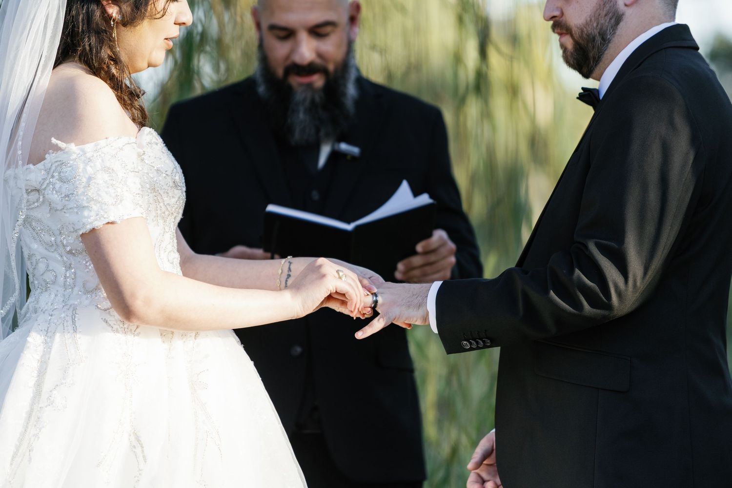 A wedding ceremony takes place outdoors with the couple and officiant standing together during the service.
