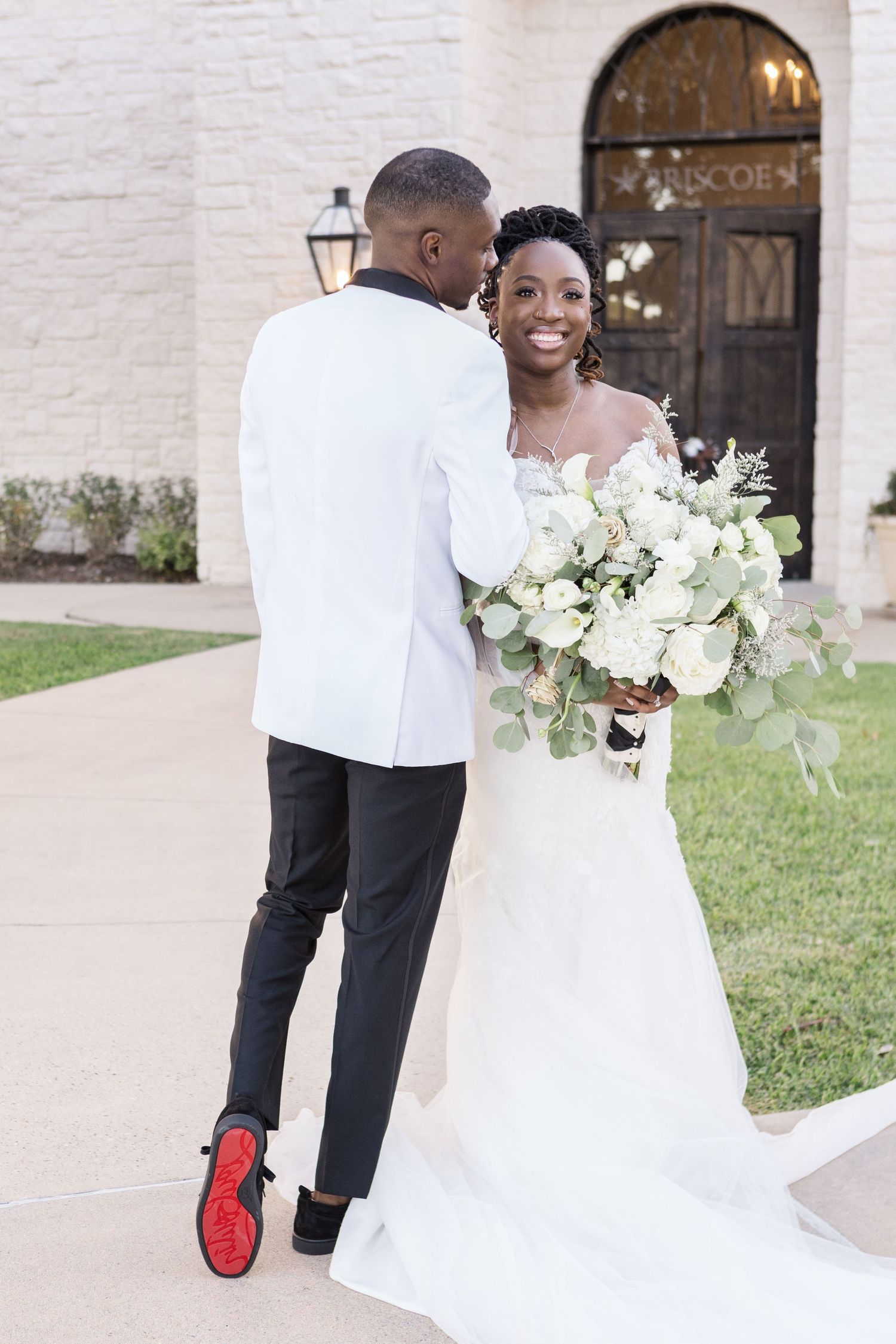 A happy couple in wedding attire shares tender moments together at their outdoor ceremony with white floral bouquets.