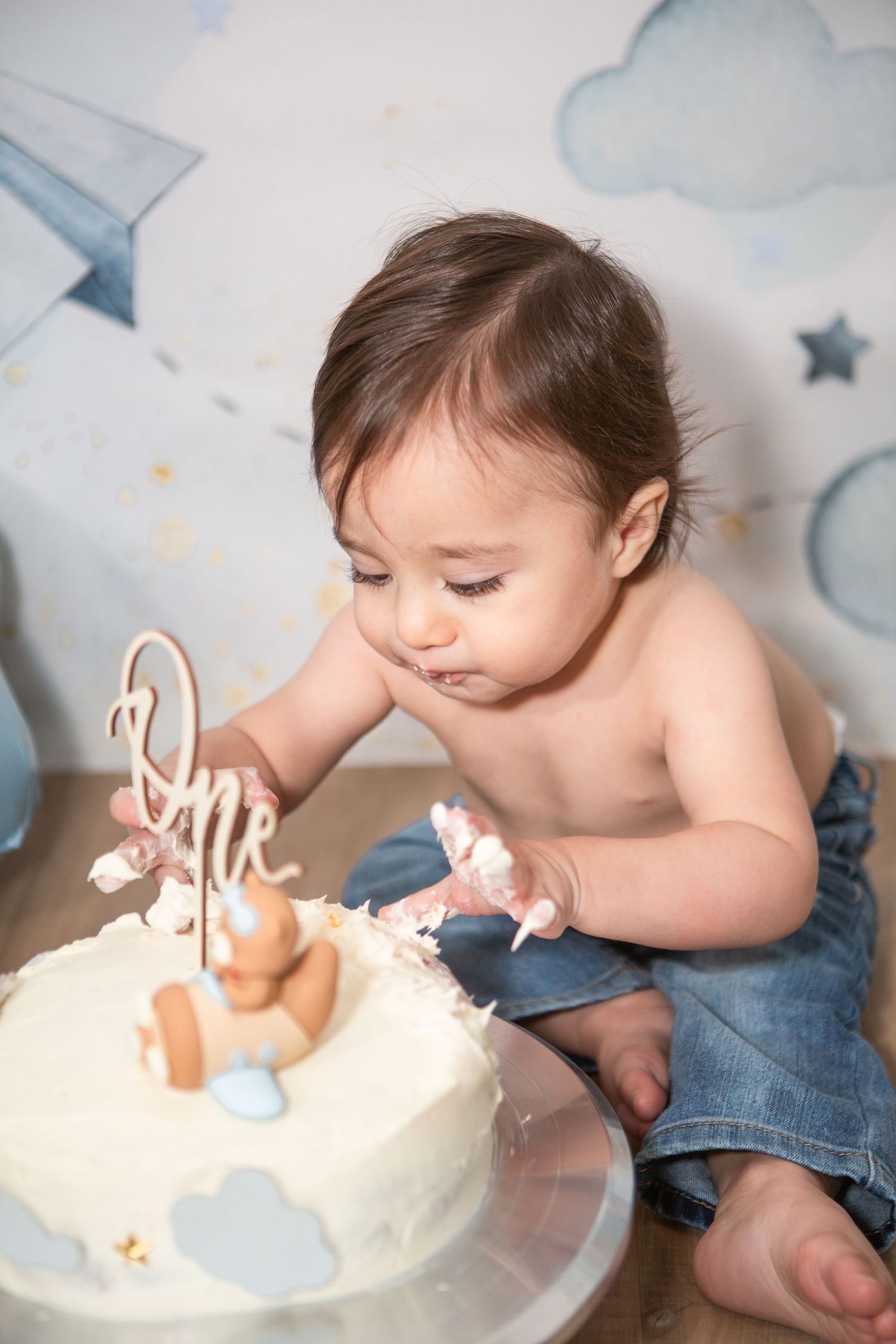 Baby reaching to touch frosting on a white birthday cake during cake smash photoshoot.