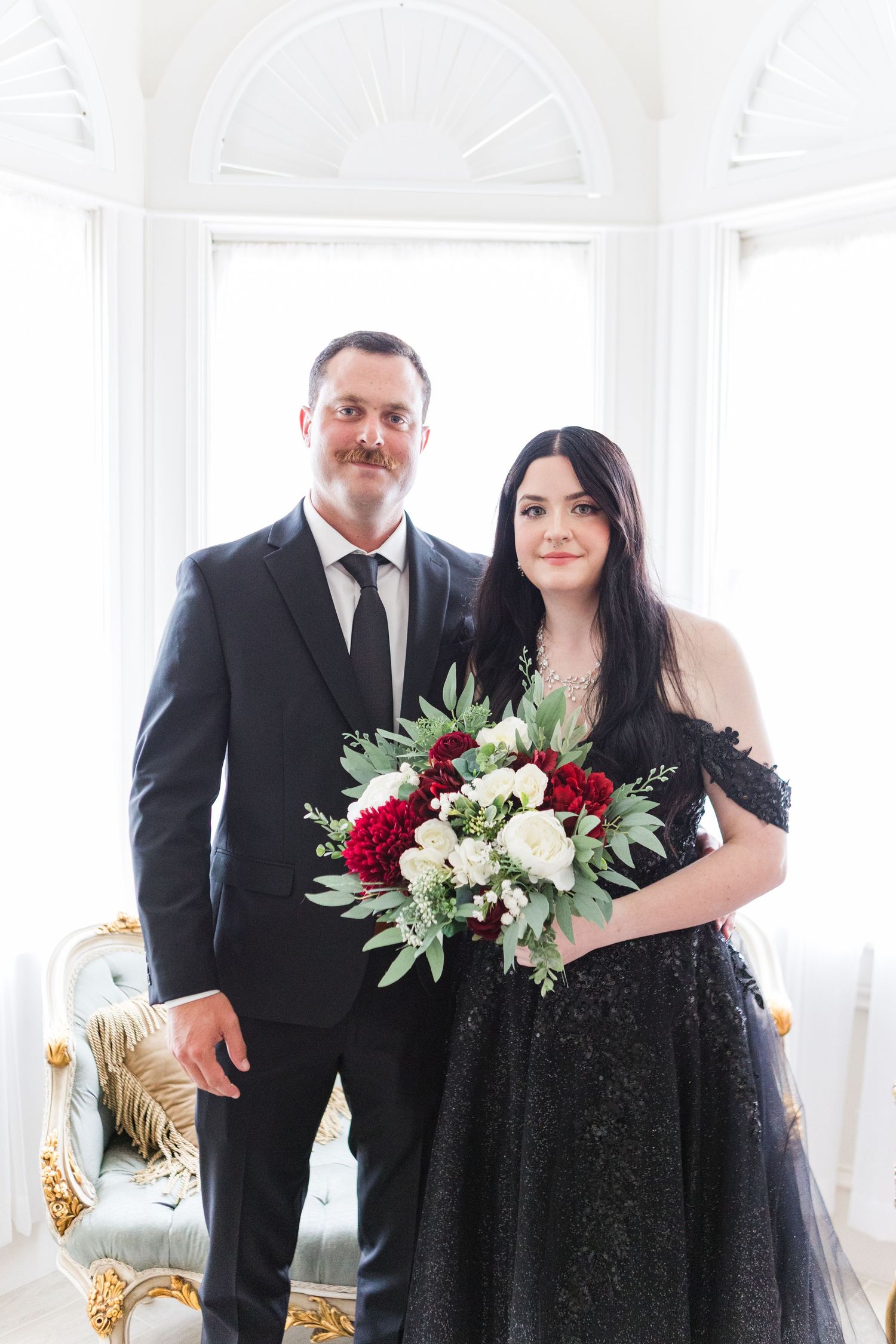 Formal portrait in bright white room with elegant black and burgundy attire.
