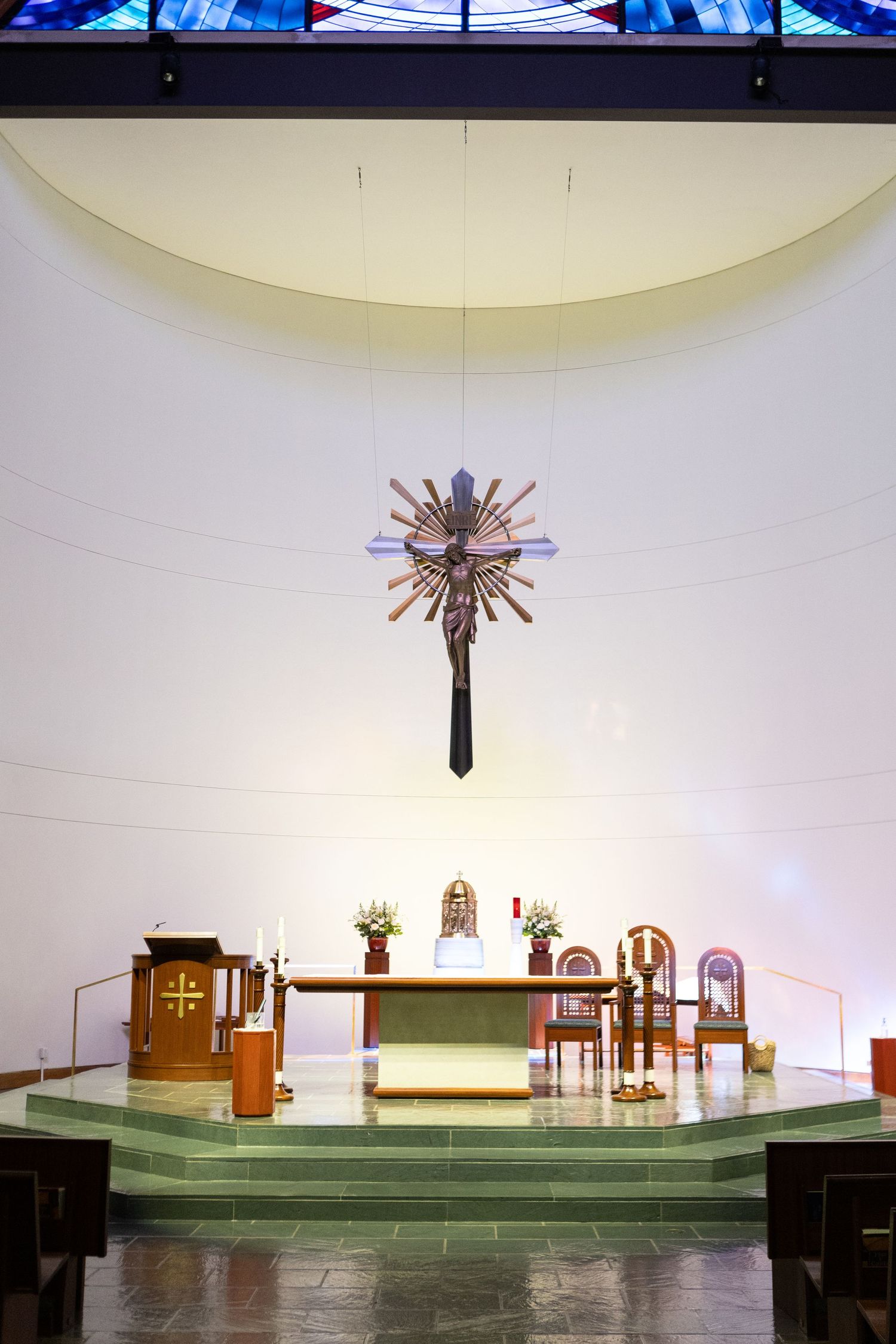 Church altar and pews arranged in a minimalist white sanctuary with decorative ceiling lighting.