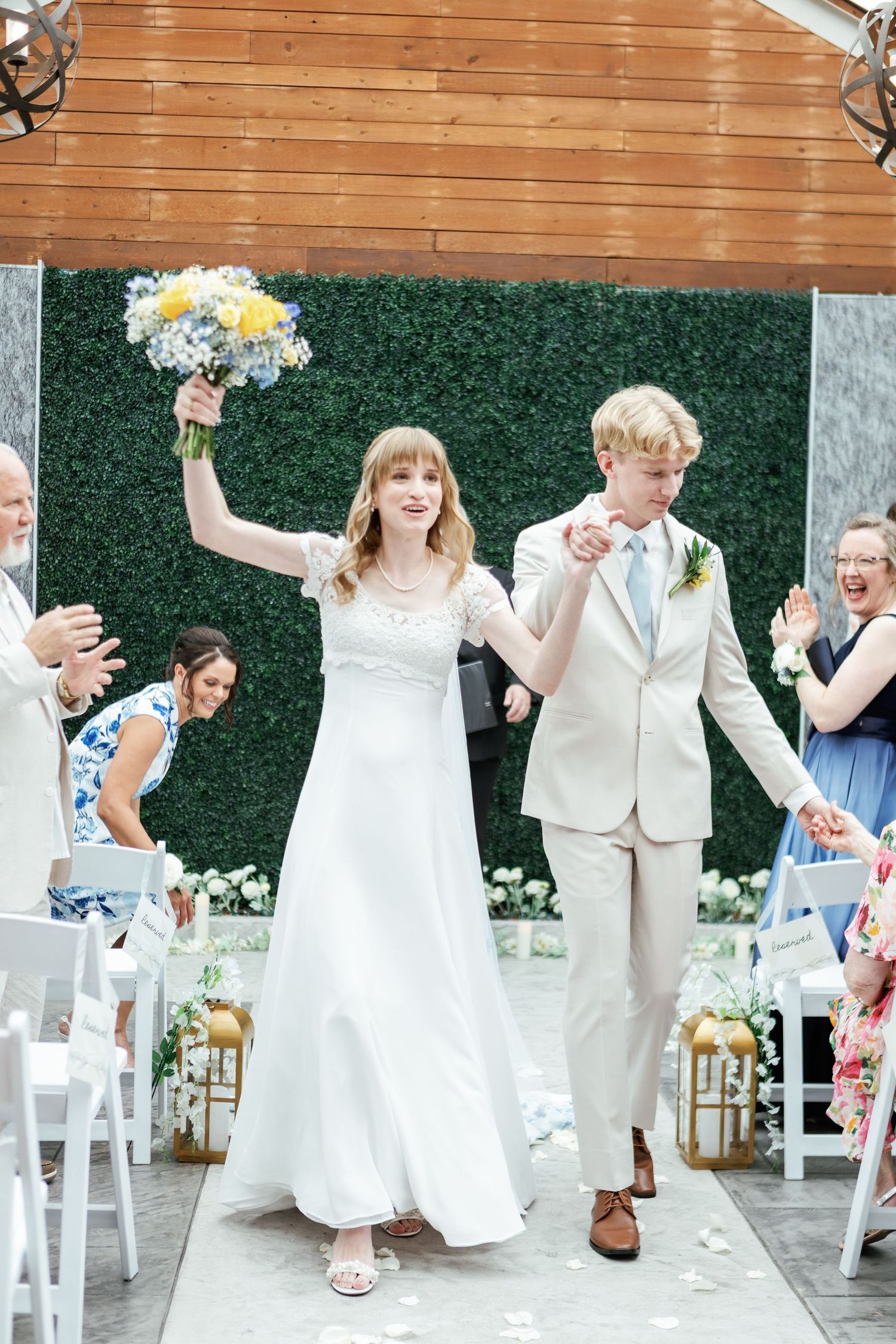 Joyful wedding celebration with couple and guests dancing under wooden pergola.