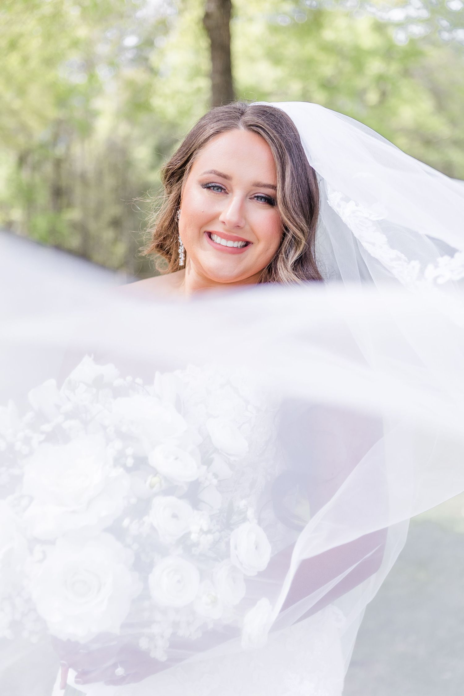 Flowing white wedding veil billowing in the breeze against a natural outdoor backdrop.