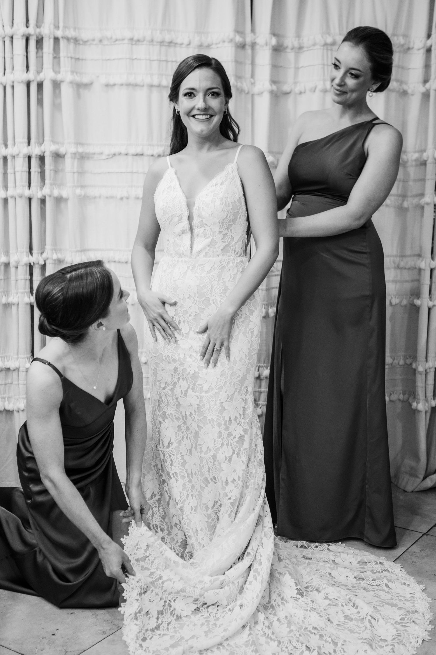 Final dress adjustments being made to a white lace wedding gown with a dramatic train.