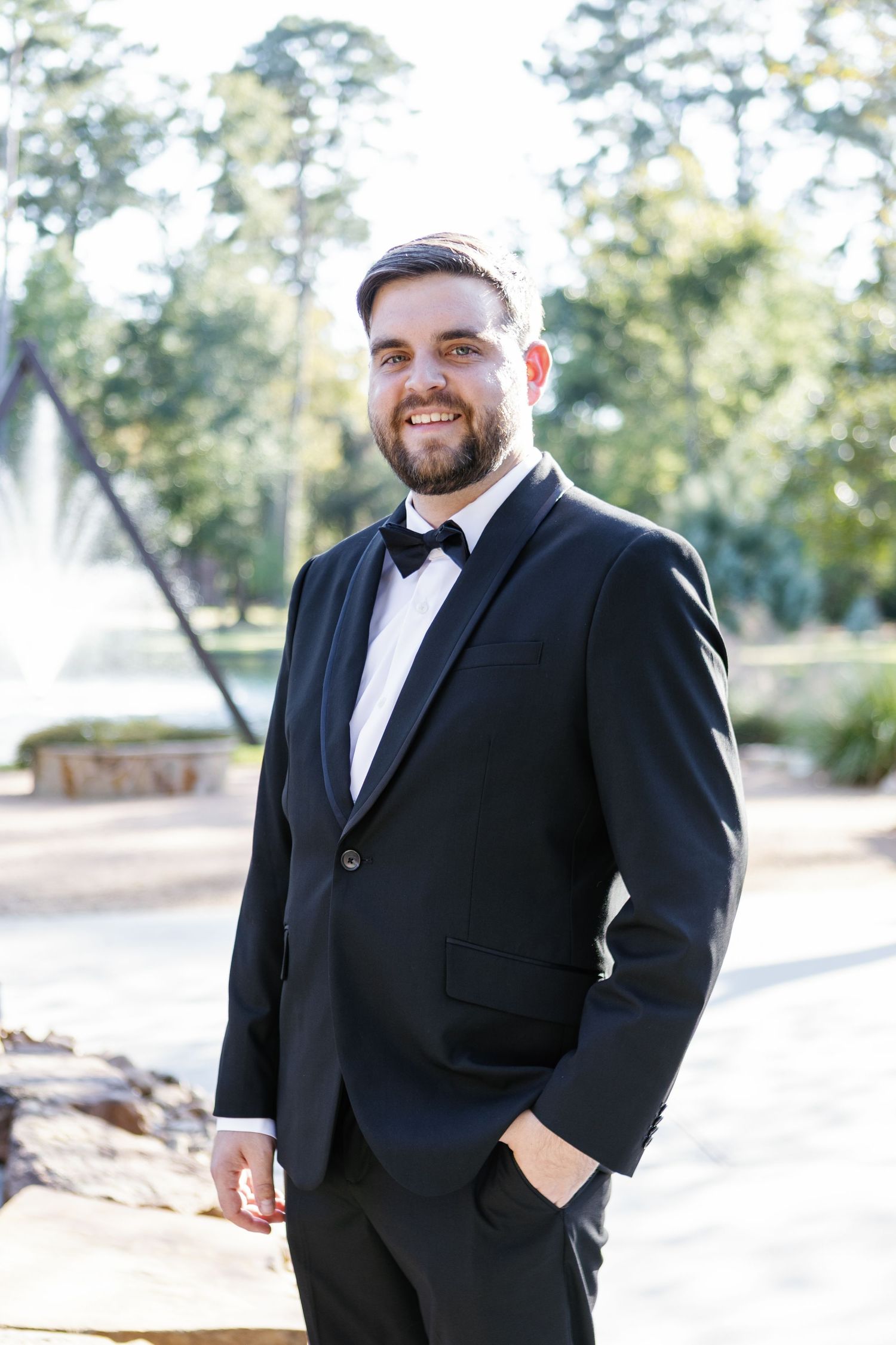 Groom in classic black tuxedo and bowtie poses outdoors on wedding day.