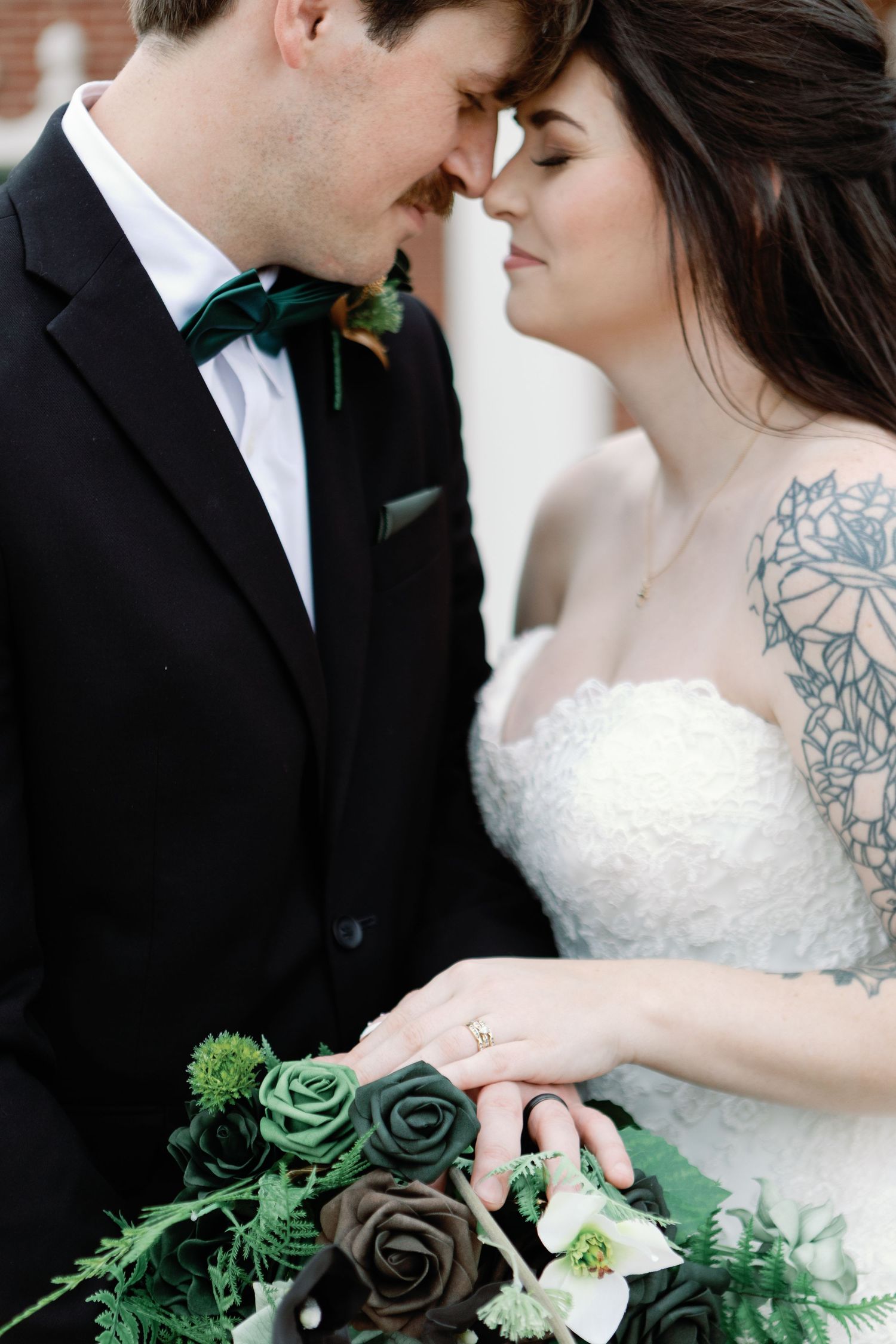 Romantic close-up of couple with bridal bouquet featuring dark roses and green foliage.