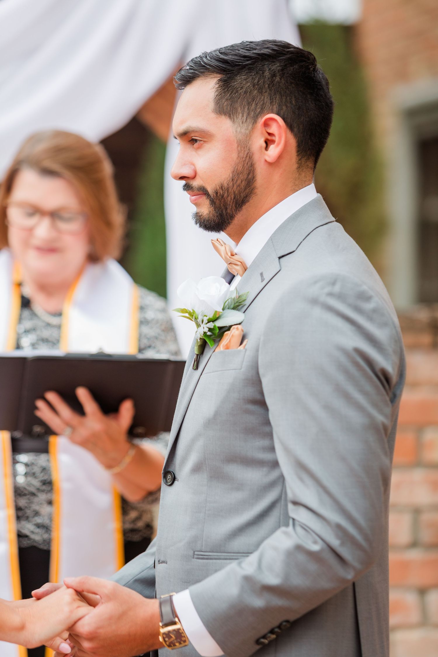 An outdoor wedding ceremony with brick walls and white draping in the background.