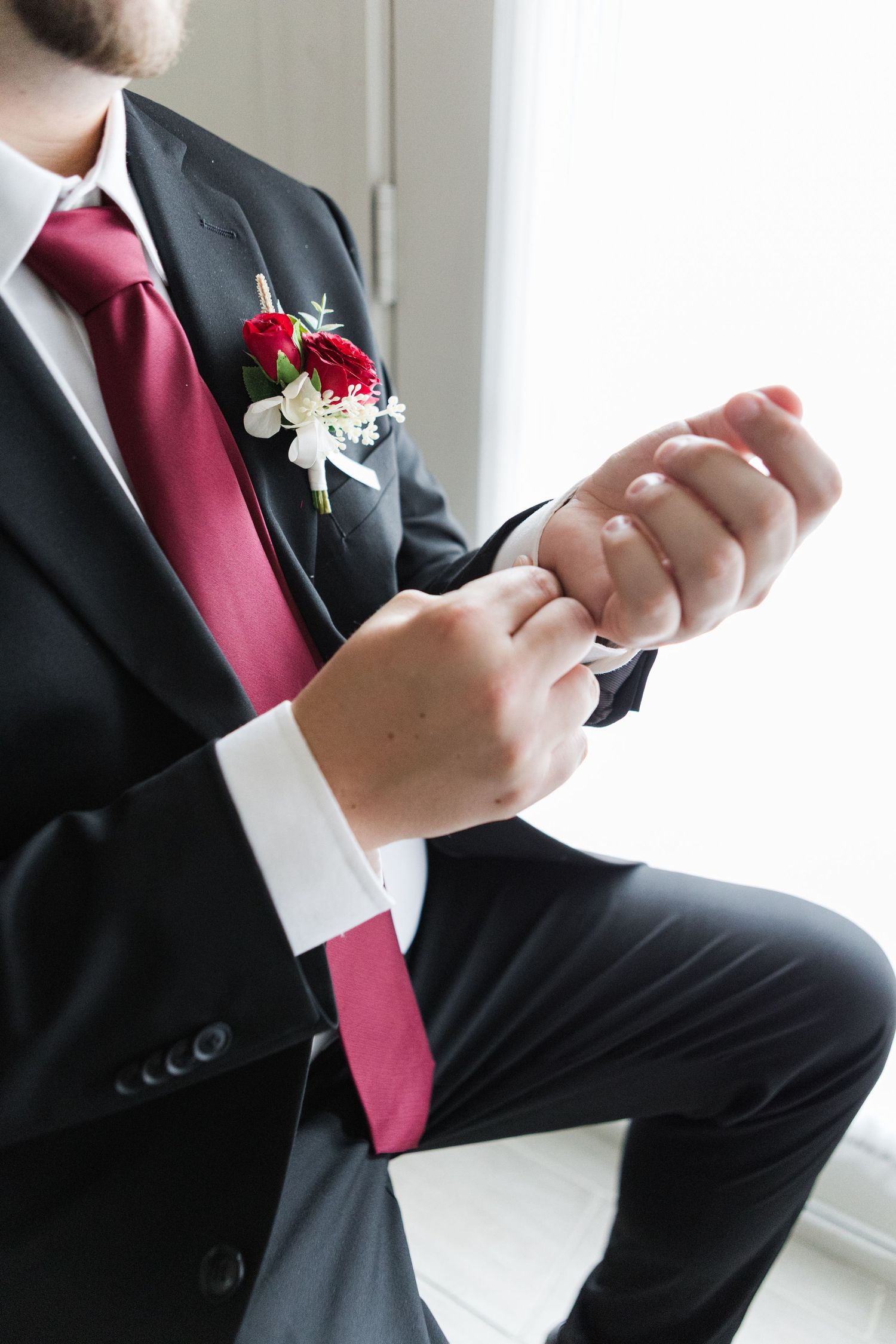 Detail shots of groom's formal wedding attire with red tie and floral boutonniere.