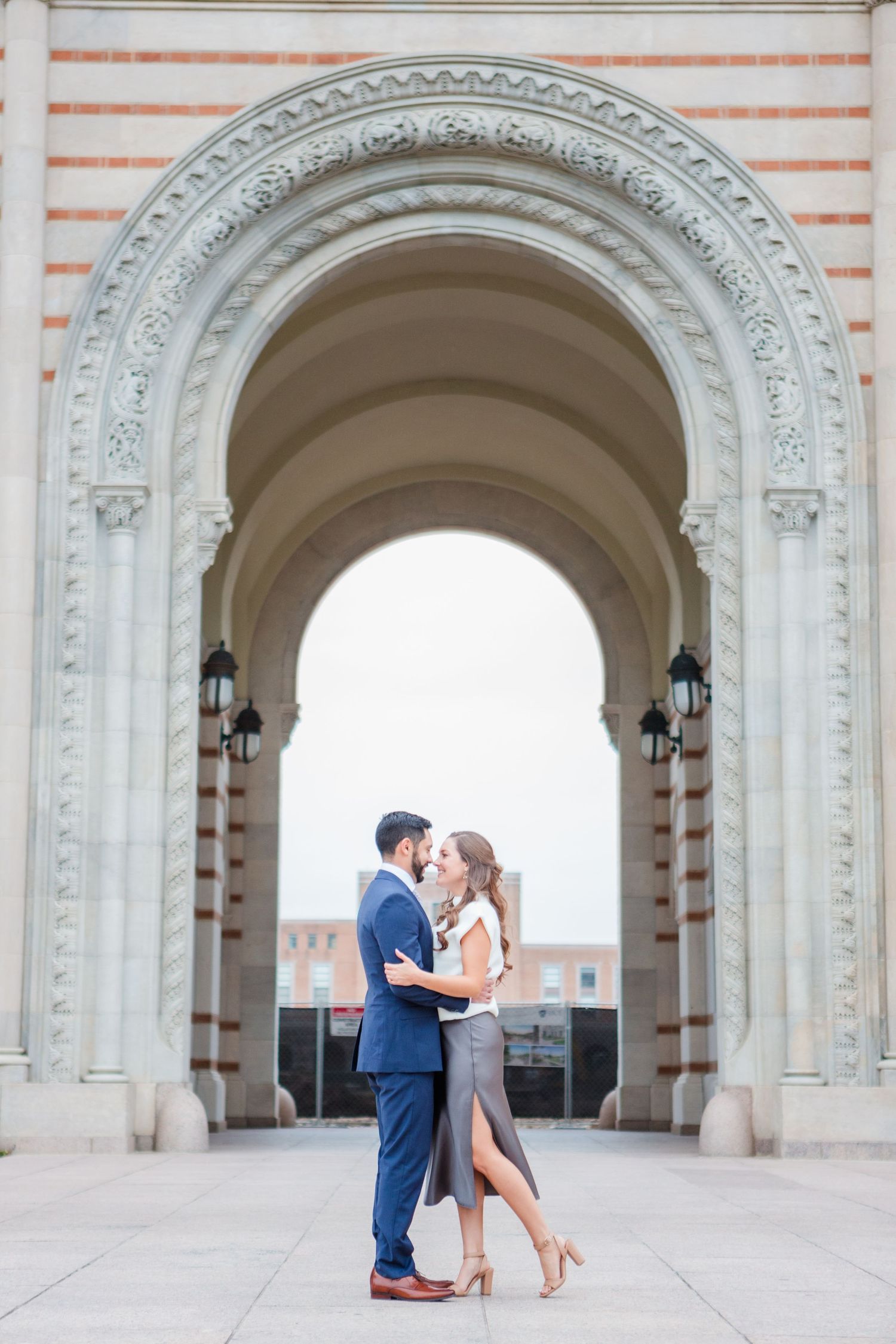 Romantic portrait of couple embracing under grand archway with decorative stonework.