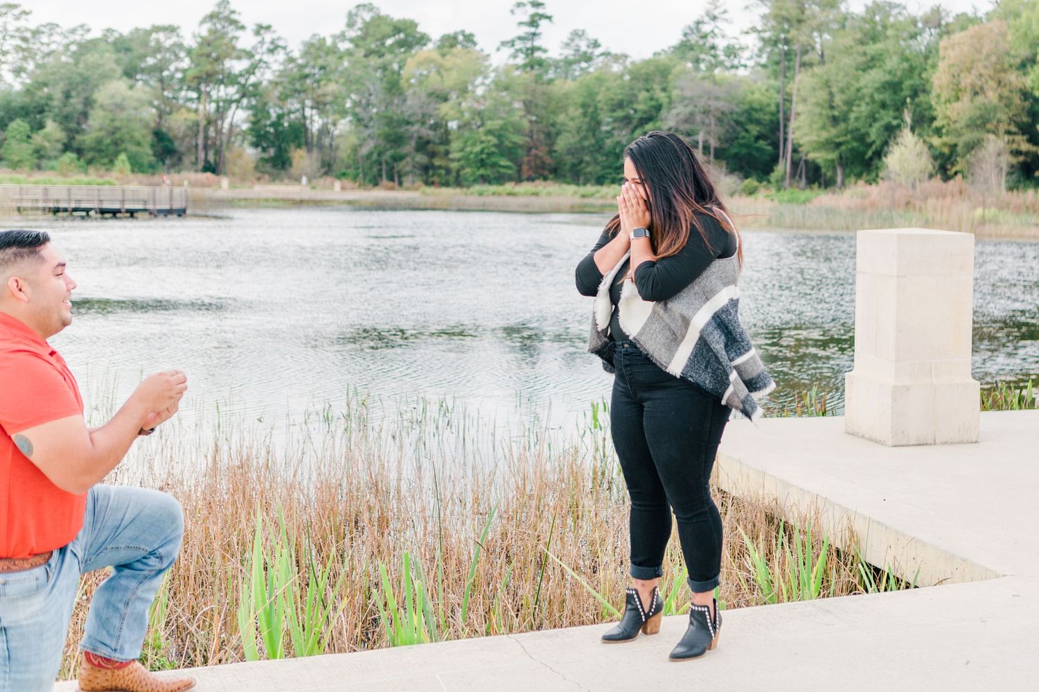 A lakeside proposal scene with someone down on one knee.