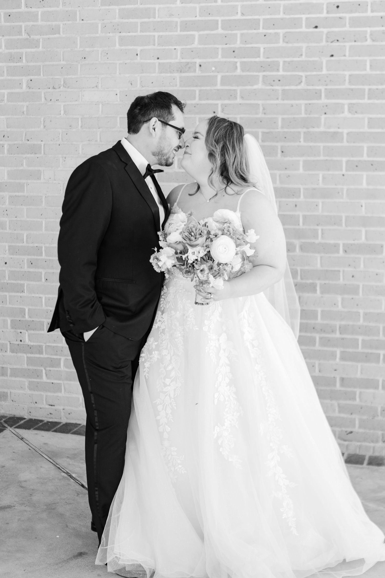 Black and white romantic wedding portraits against industrial brick wall backdrop.