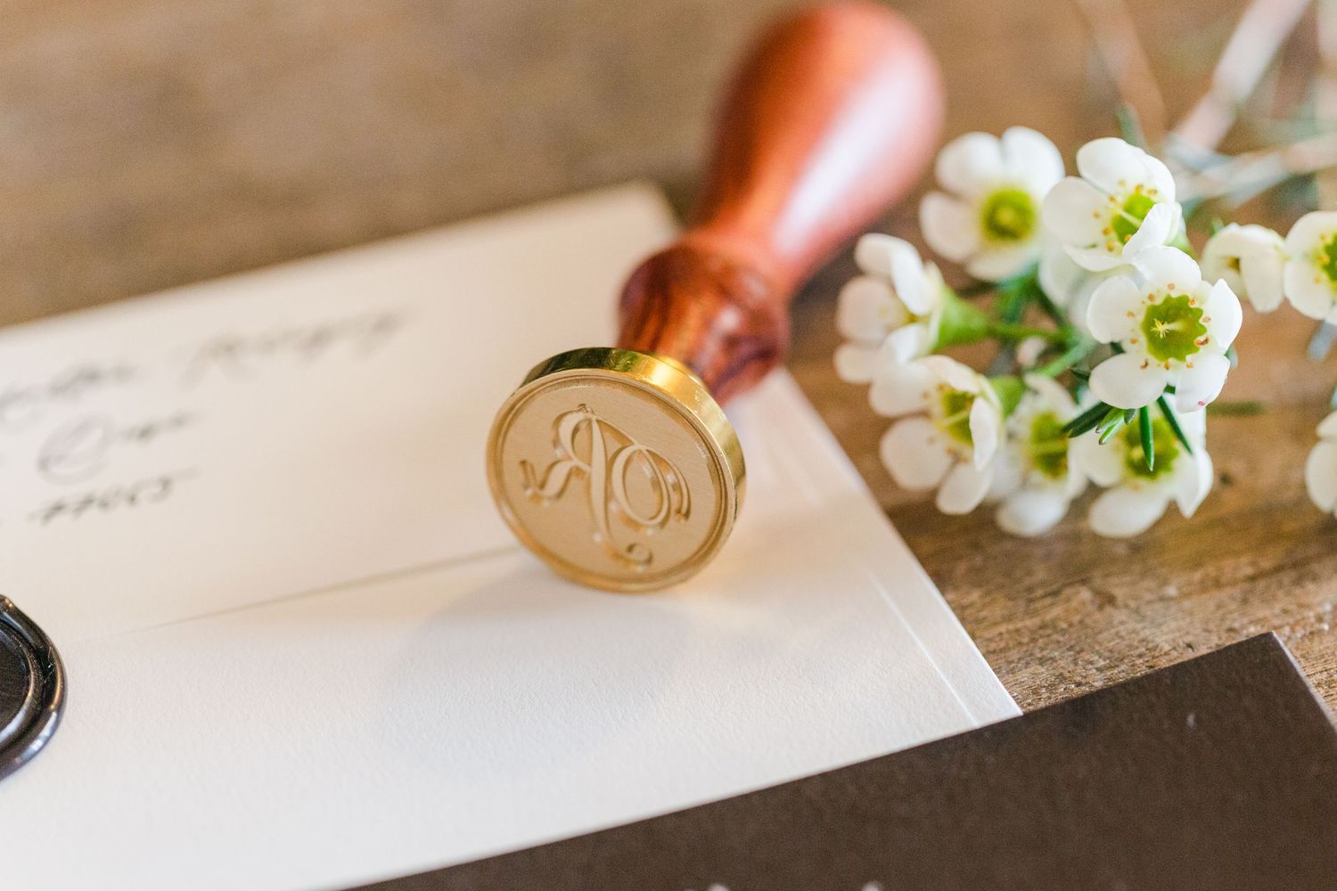 Wedding invitation suite with wax seals and white flowers on wooden table surface.