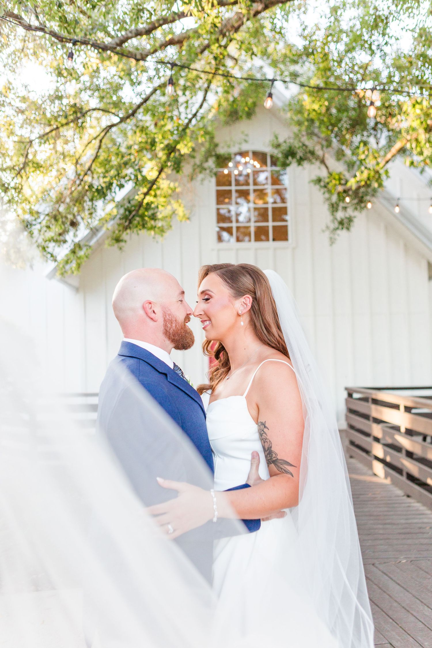 Couple sharing tender moments during wedding photoshoot under tree branches.