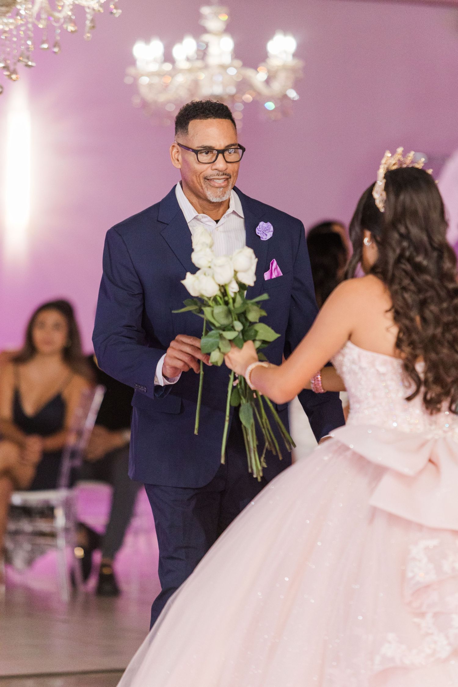 Formal dance exchange with white roses in an elegant purple-lit venue during a celebration.