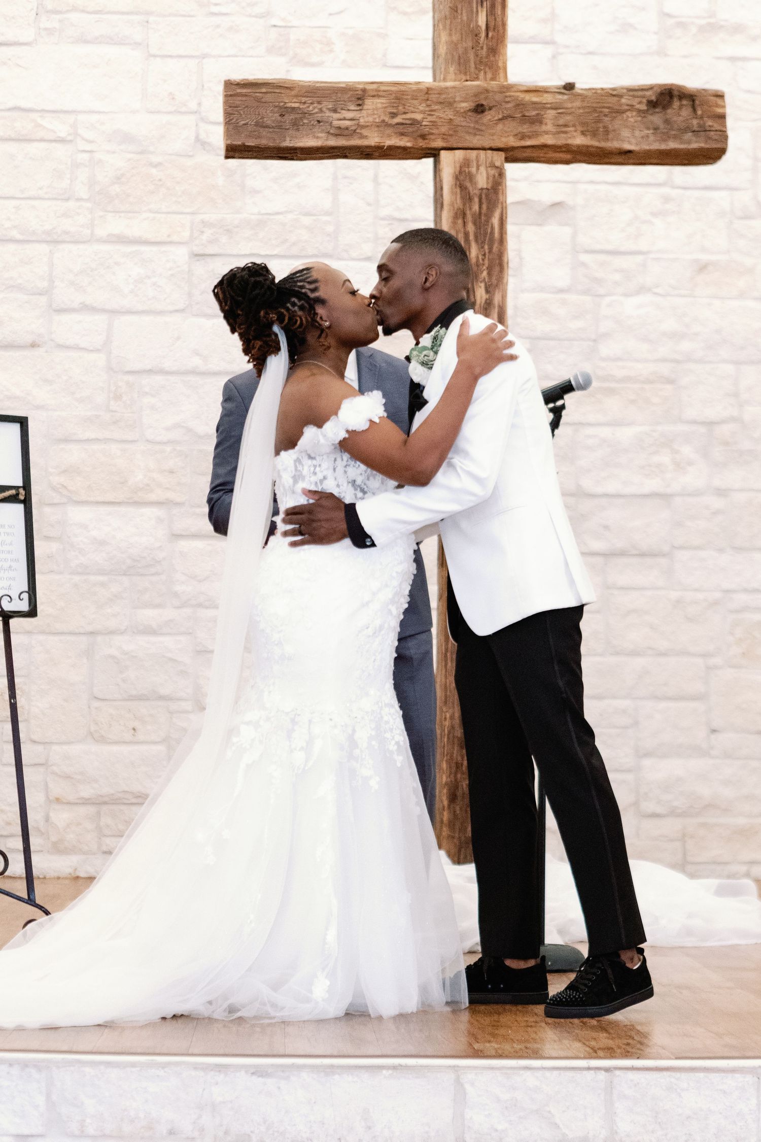 A newly married couple share a romantic kiss in front of a wooden cross during their wedding ceremony.