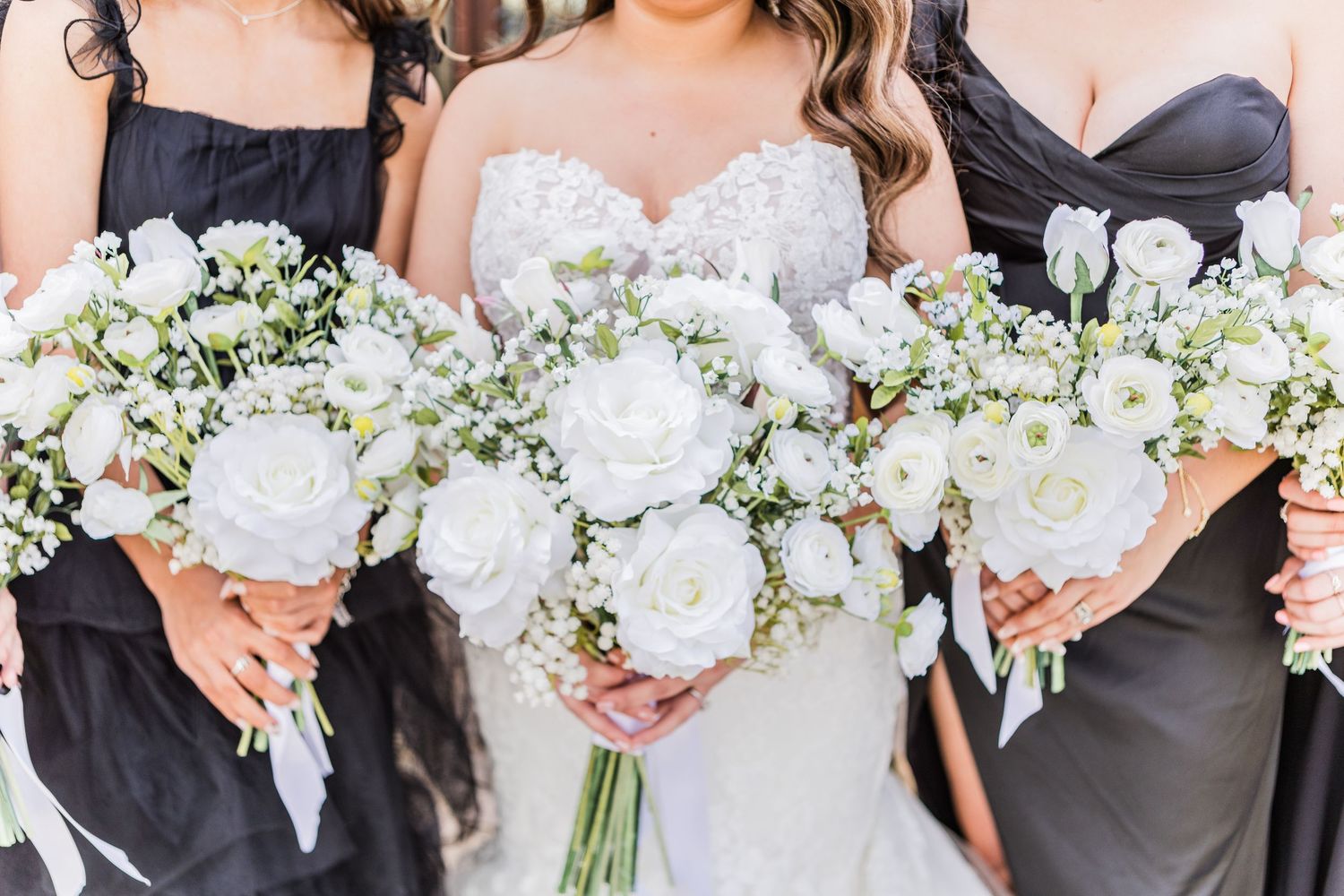 Bridesmaids in black dresses holding white floral bouquets in a row.