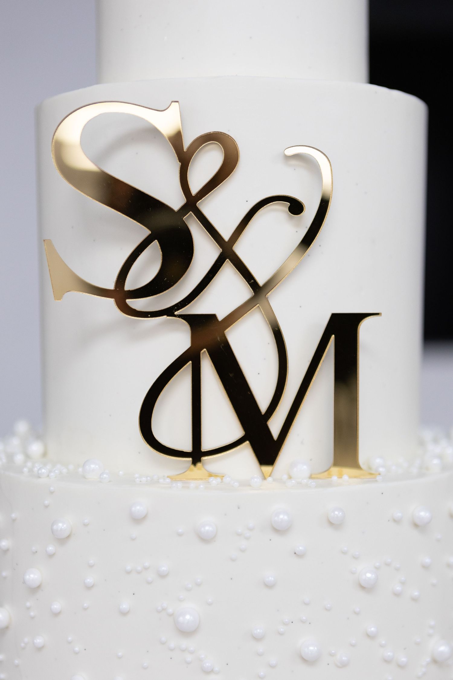 Close-up of gold metallic monogram design on white wedding cake tier.
