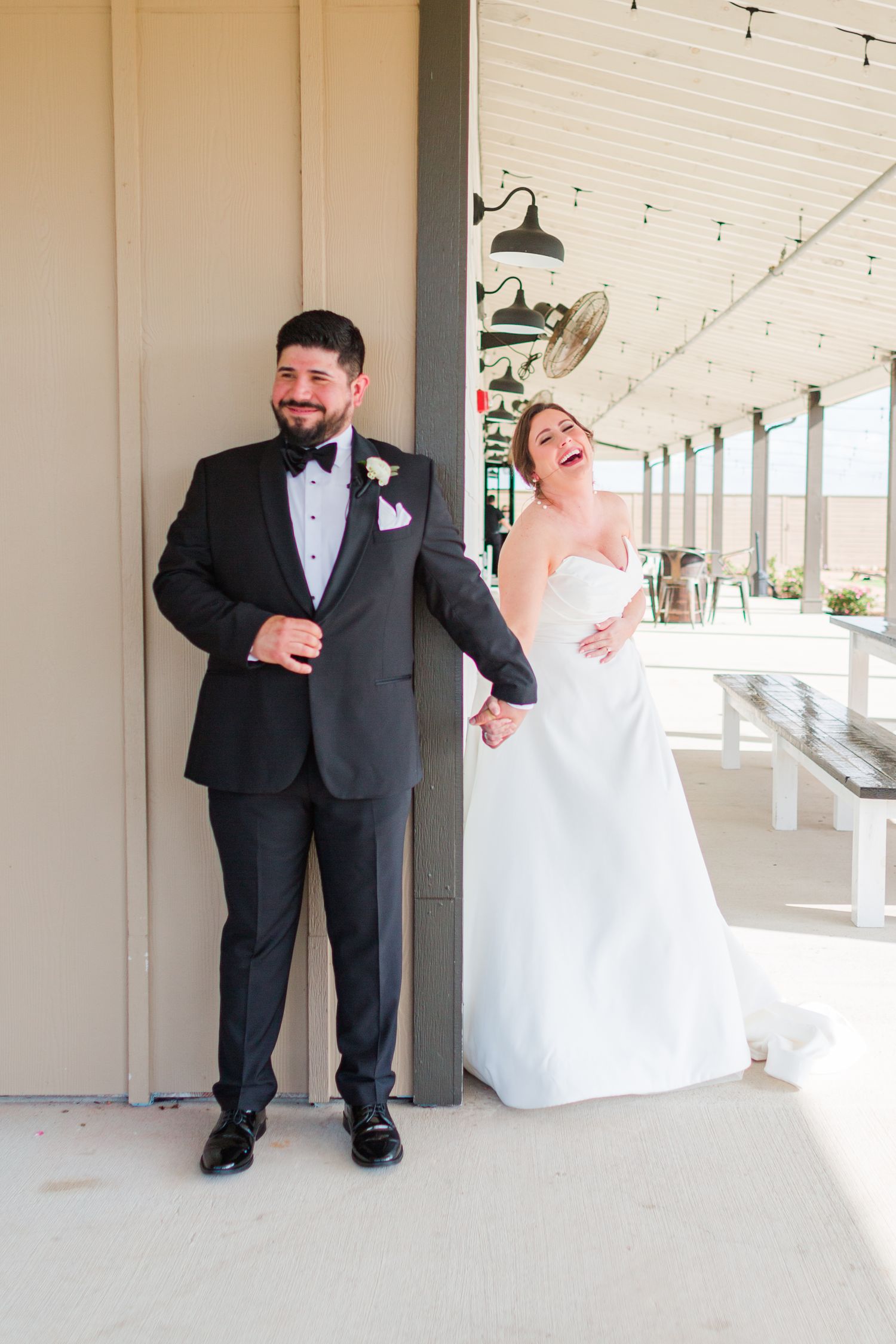 Bride and groom share laughter during their first look photo series on a covered porch.
